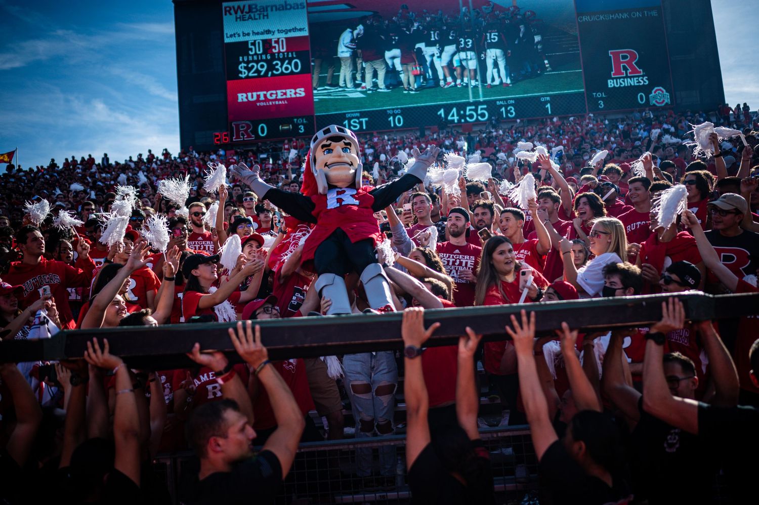 A large crowd of fans at a stadium raises their arms in unison during an exciting sporting event.