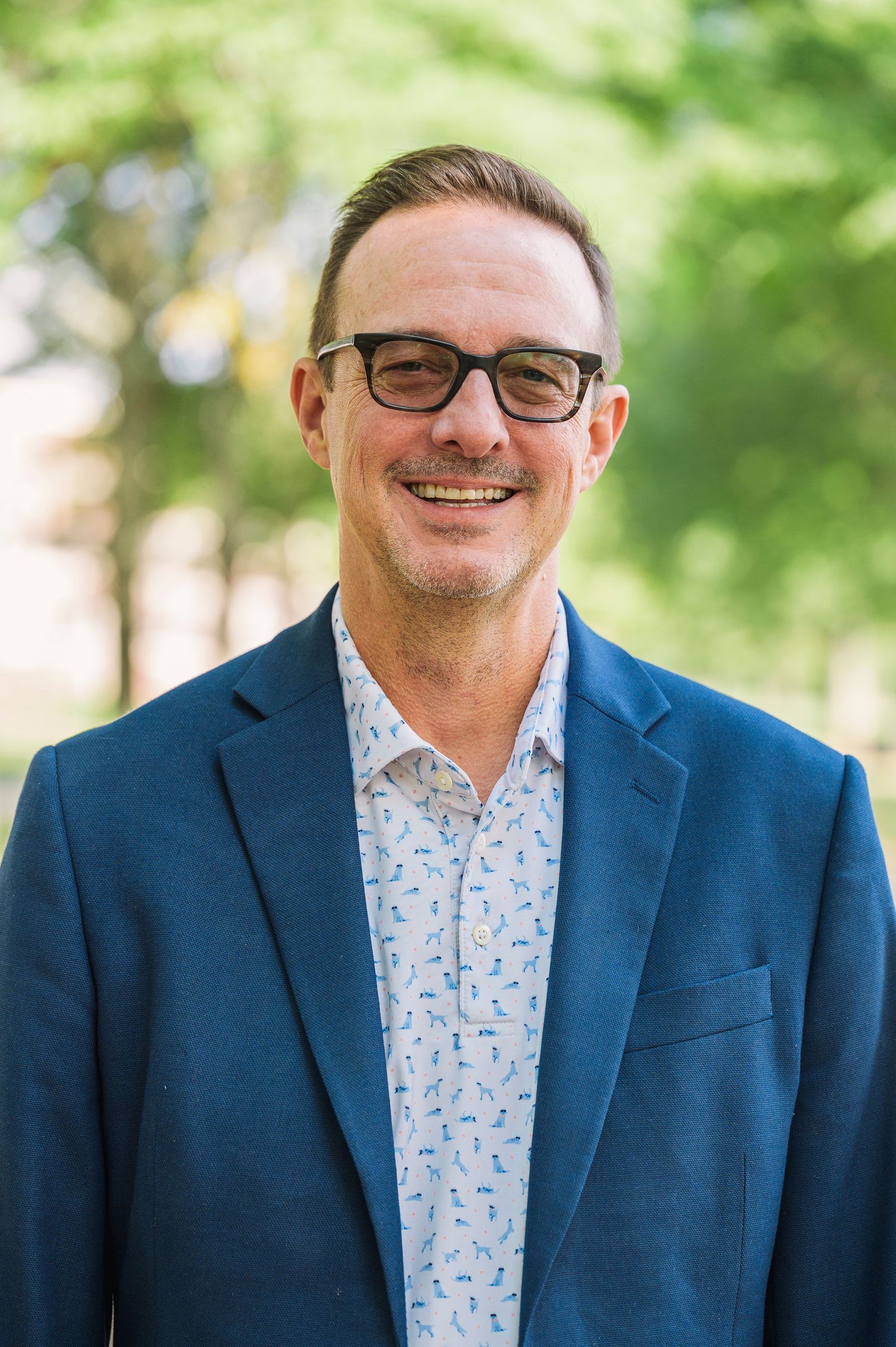 Professional headshots of person in blue blazer and patterned shirt against green background.