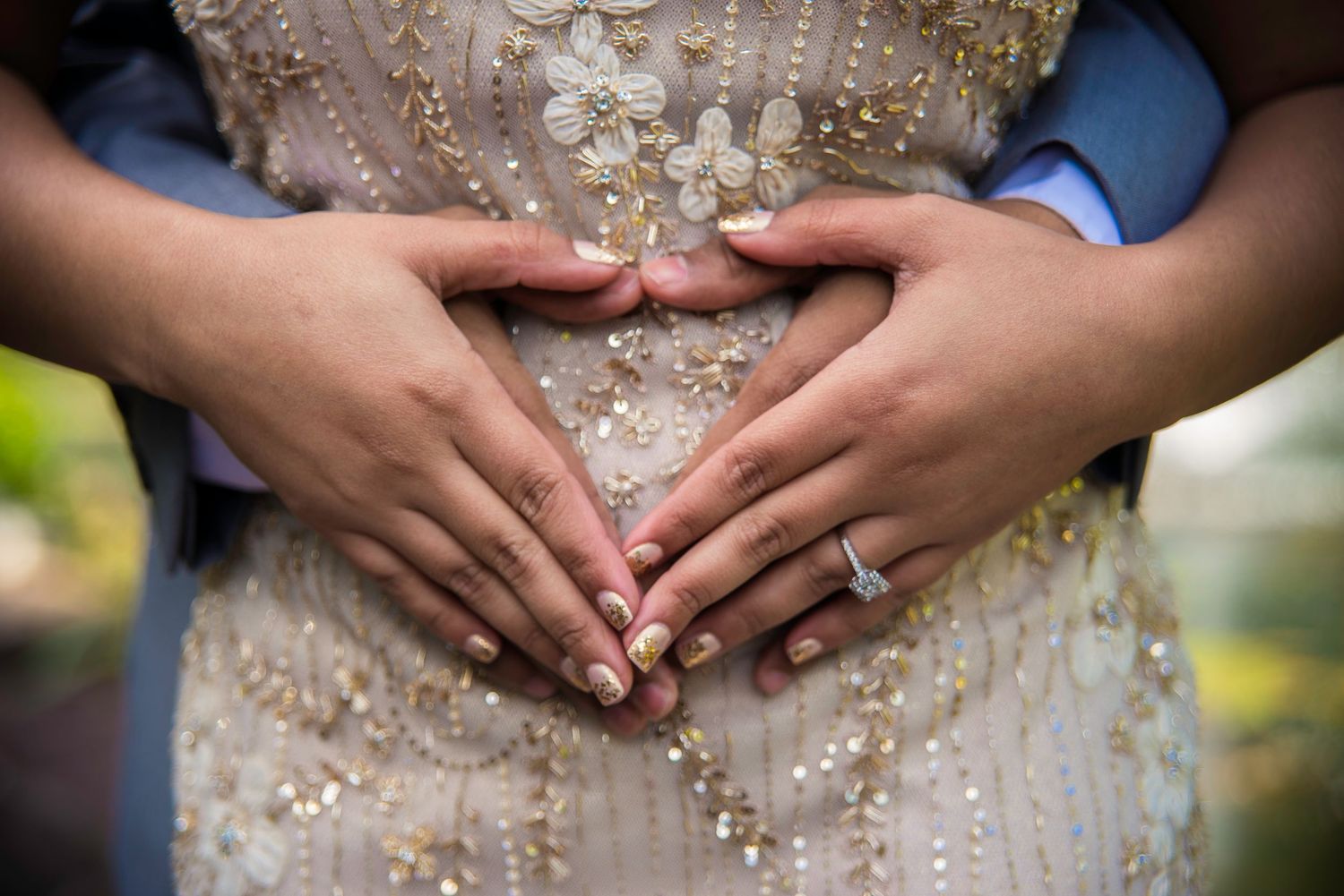 Close-up detail of hands resting on an ornate beaded wedding dress with sparkling crystal embellishments.