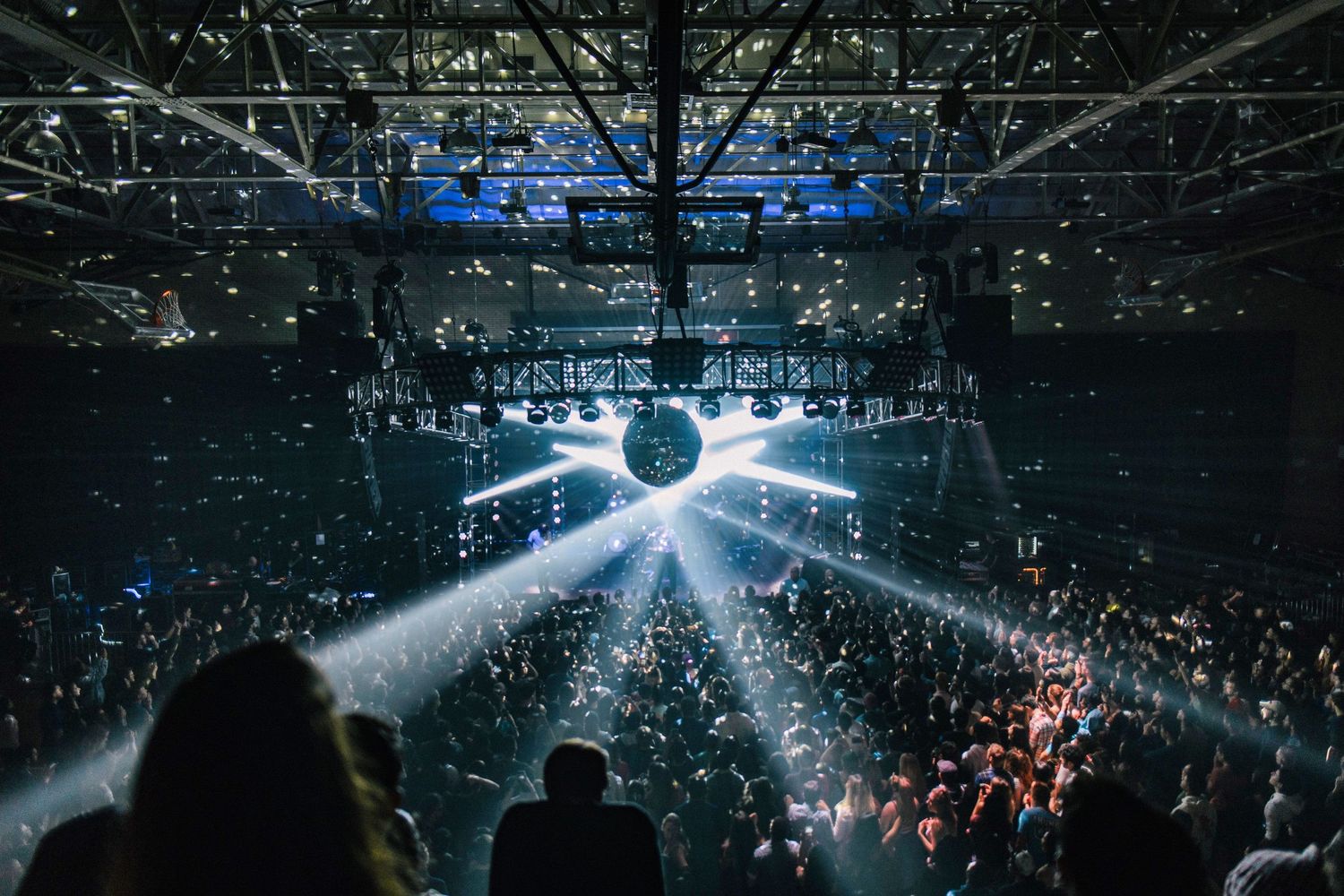 Large concert arena filled with spectators under dramatic spotlights and beams of light creating an atmospheric ambiance.