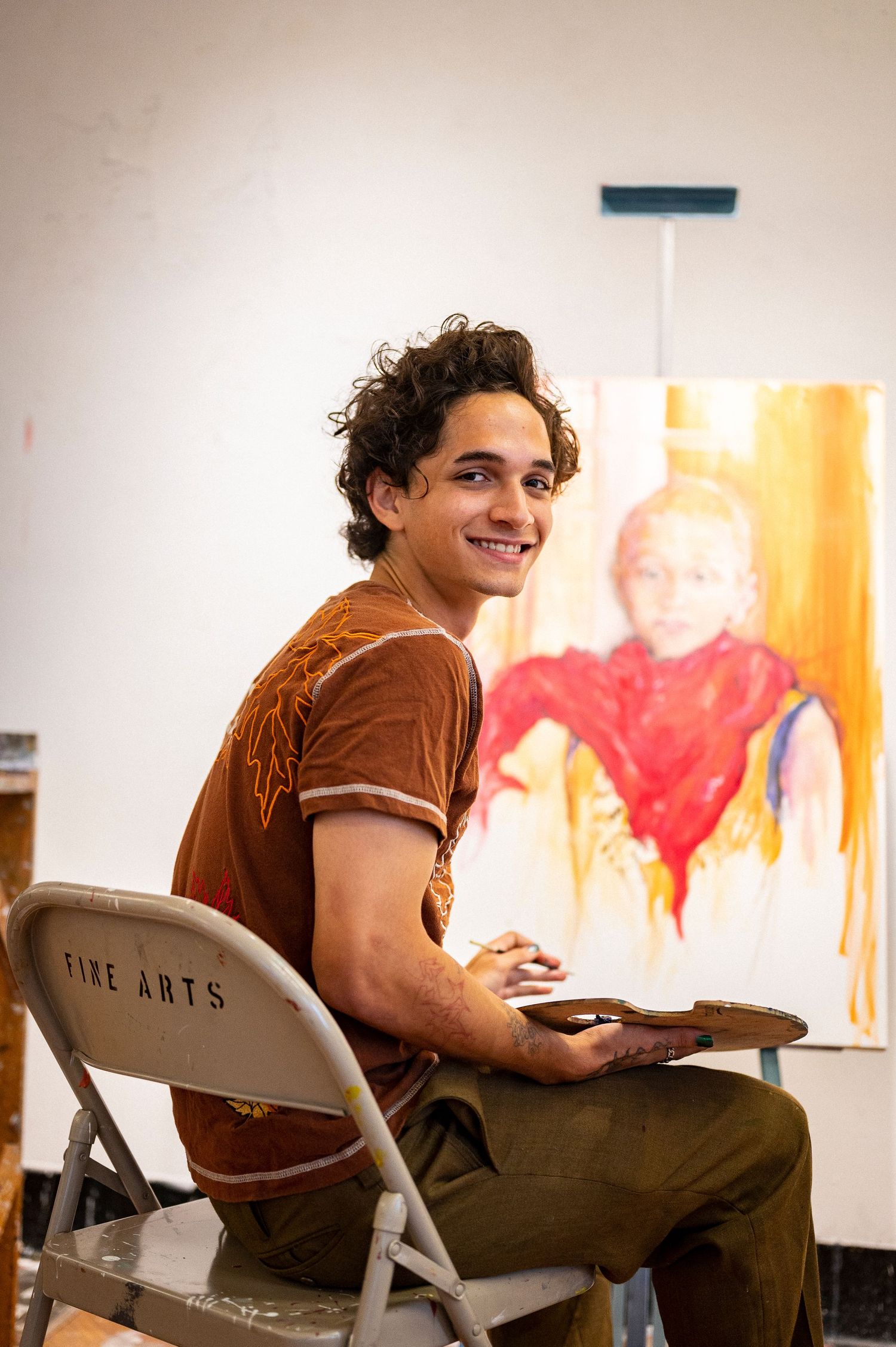 Student sitting in art classroom with colorful artwork displayed on wall.