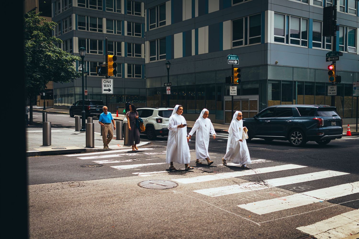 Urban street scene with crosswalk and buildings showing pedestrians crossing in white clothing.