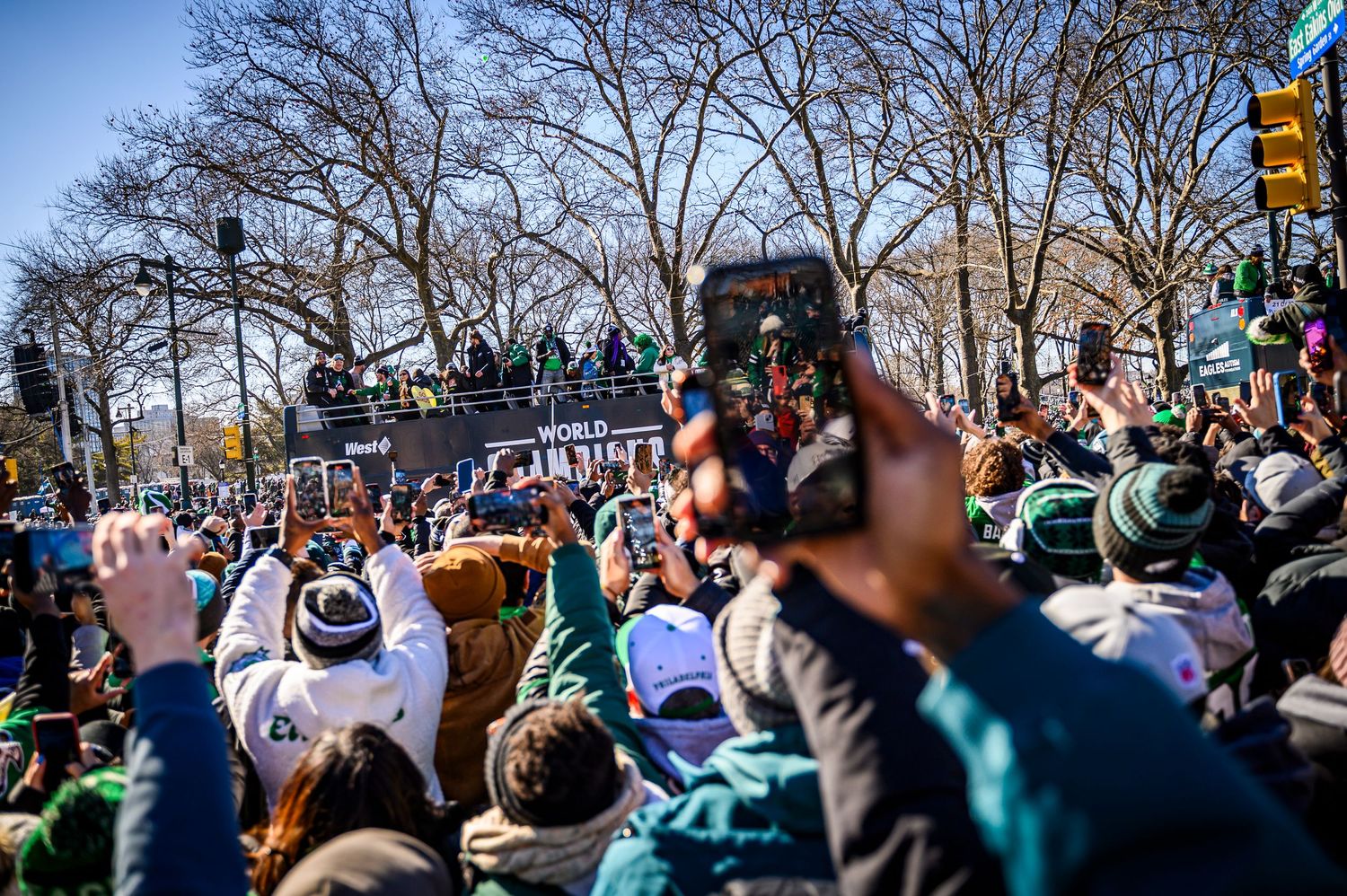Large crowd gathers at outdoor event in park with bare winter trees visible in background.