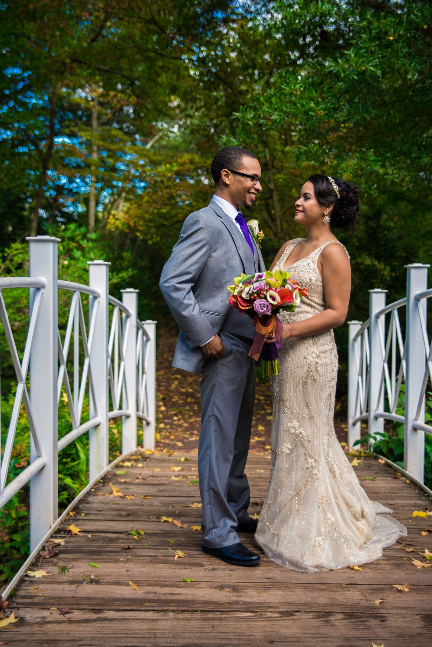 Wedding couple posing on a white wooden bridge surrounded by autumn foliage.