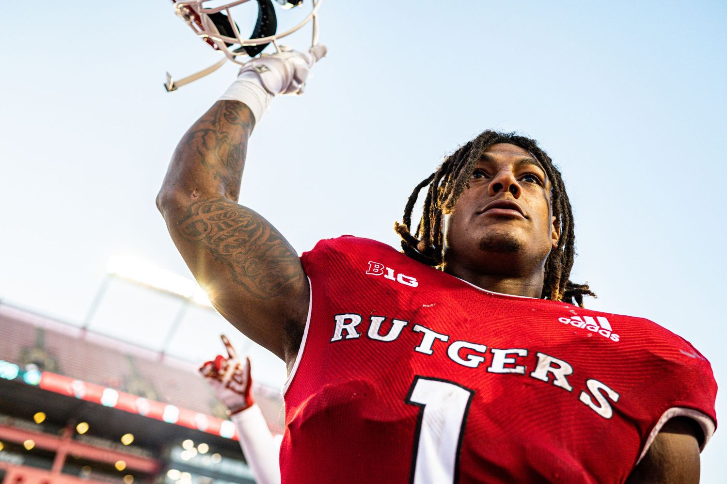 A football player in a red Rutgers jersey number 1 celebrates with raised arms in a stadium.