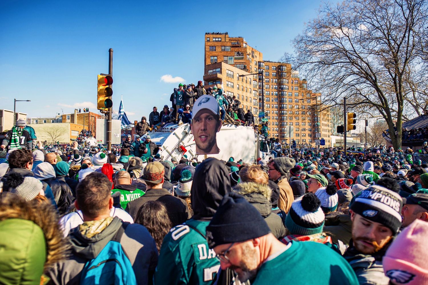 Large crowd of spectators gathers along a city street during a public event on a sunny winter day.