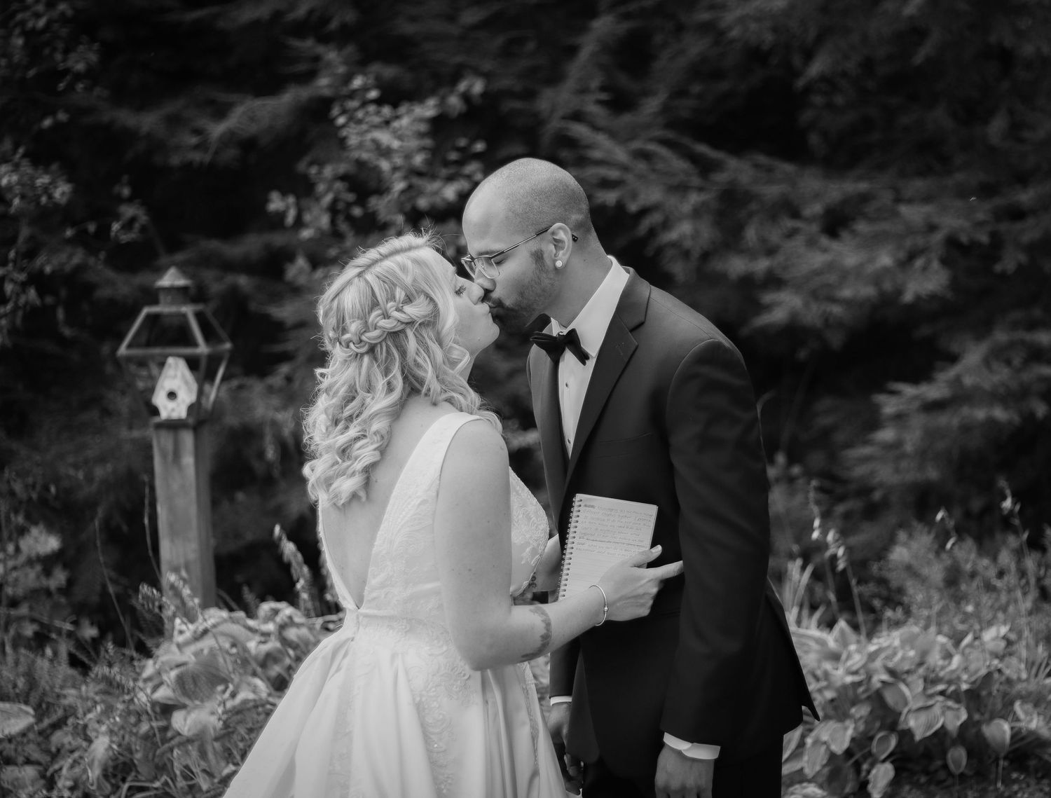Romantic wedding moment captured in black and white among garden foliage.