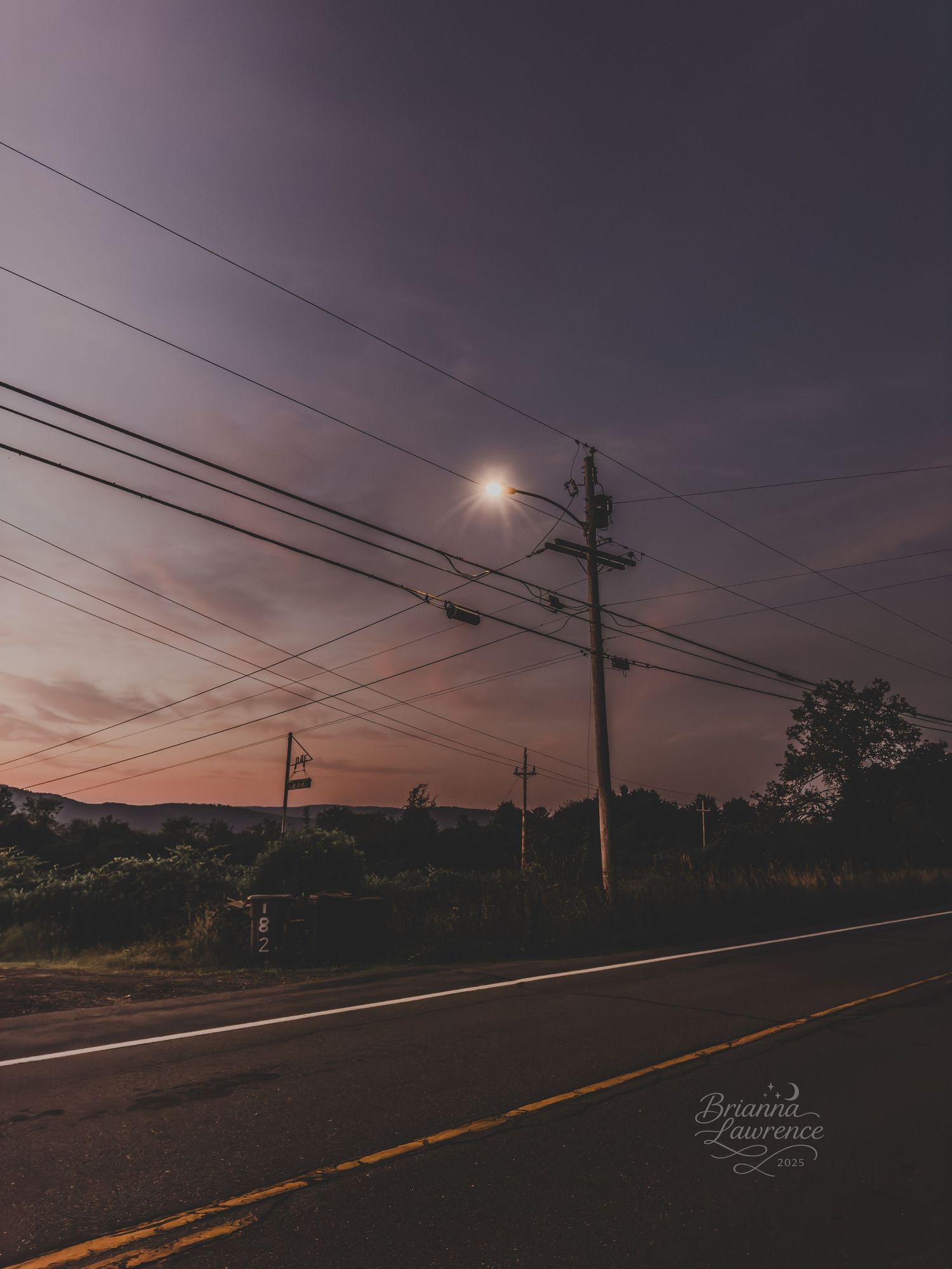 A moody sunset view of utility poles and power lines stretching along a rural road.