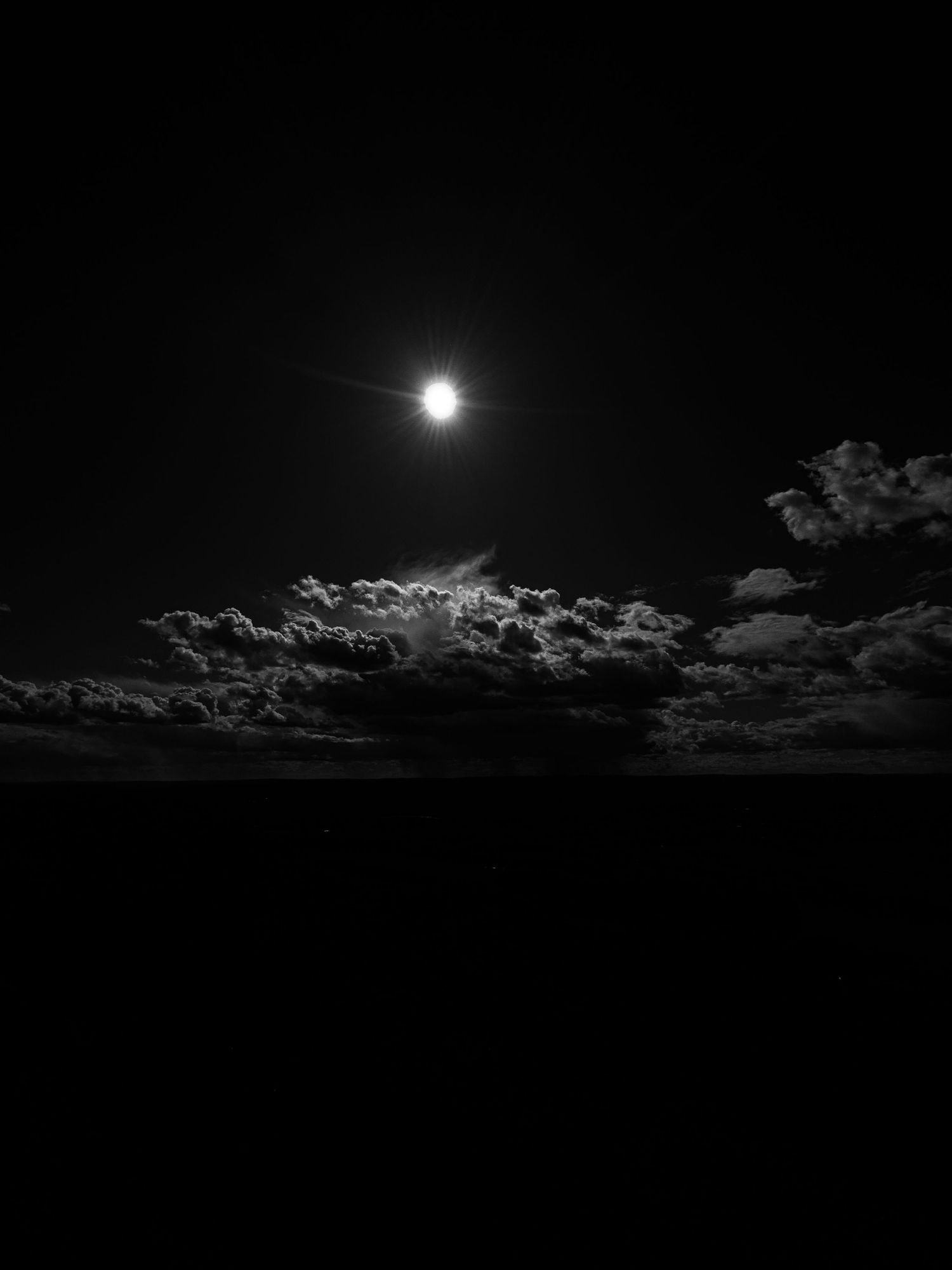Bright full sun illuminating a darkened sky with scattered clouds.