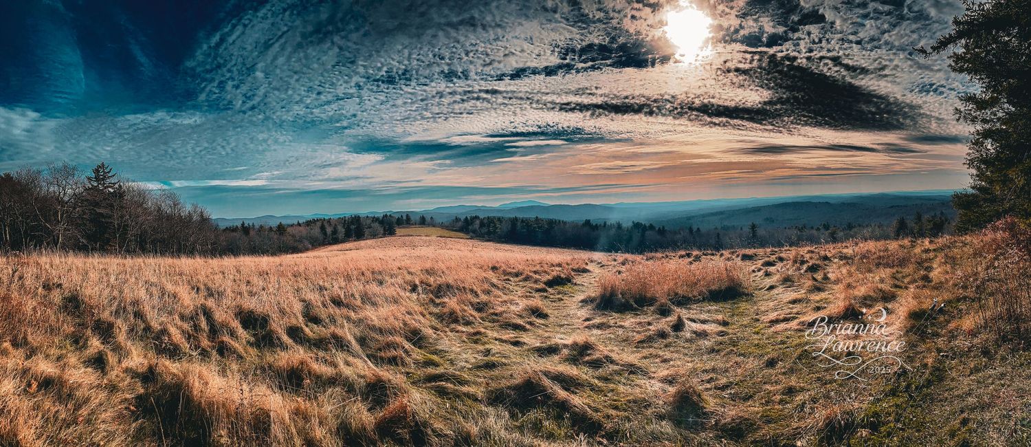 Panoramic vista of rolling hills and mountains under a bright blue sky.