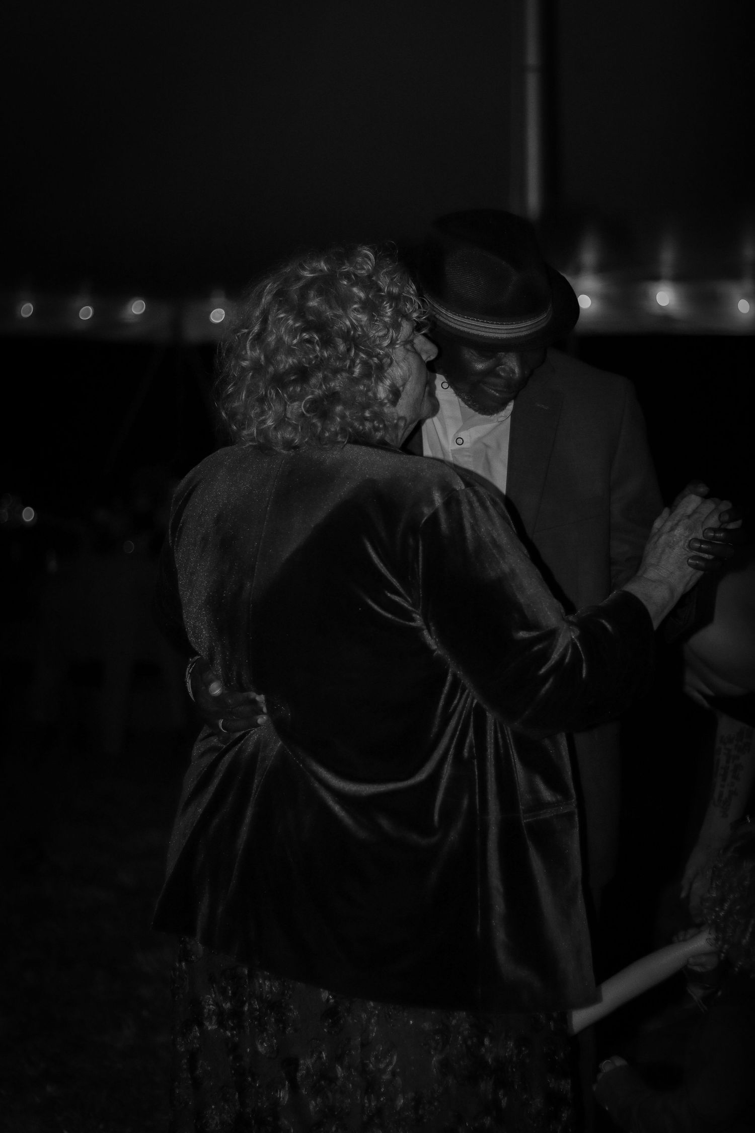 Dark evening wedding gathering with people embracing in formal attire.