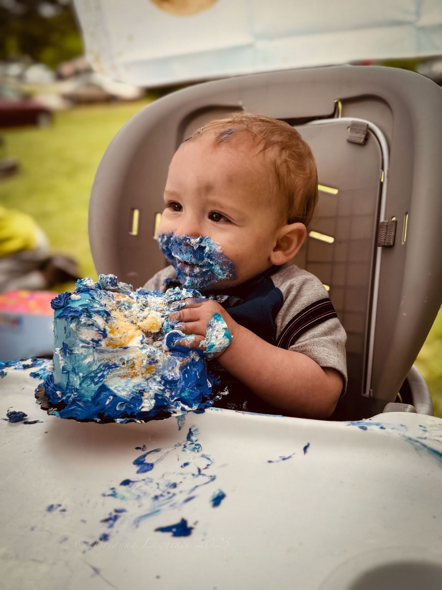 Baby in high chair enjoying messy first birthday cake smash with blue frosting.