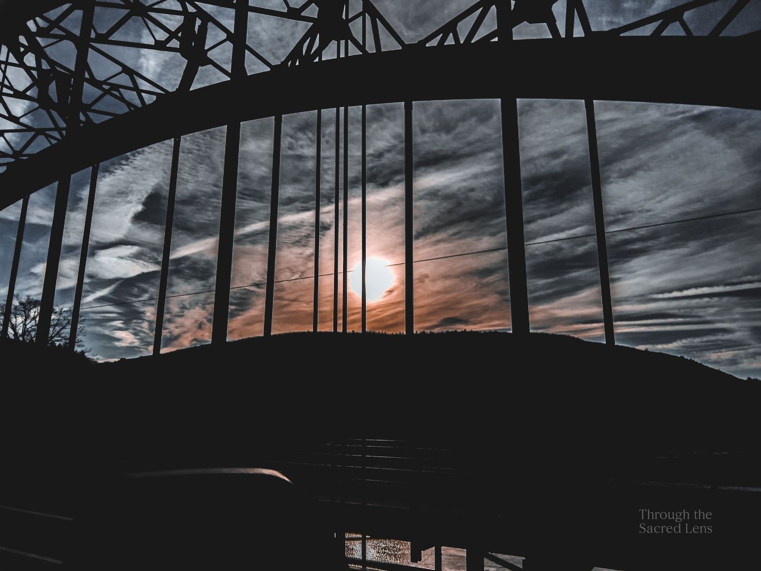 Silhouette of bridge architecture against dramatic sunset sky with streaking clouds.