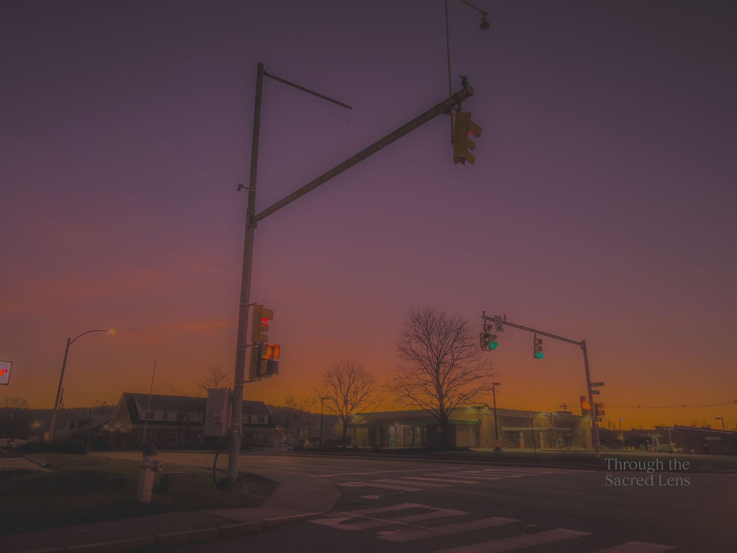 Traffic lights and street poles silhouetted against a vibrant purple and orange sunset sky.