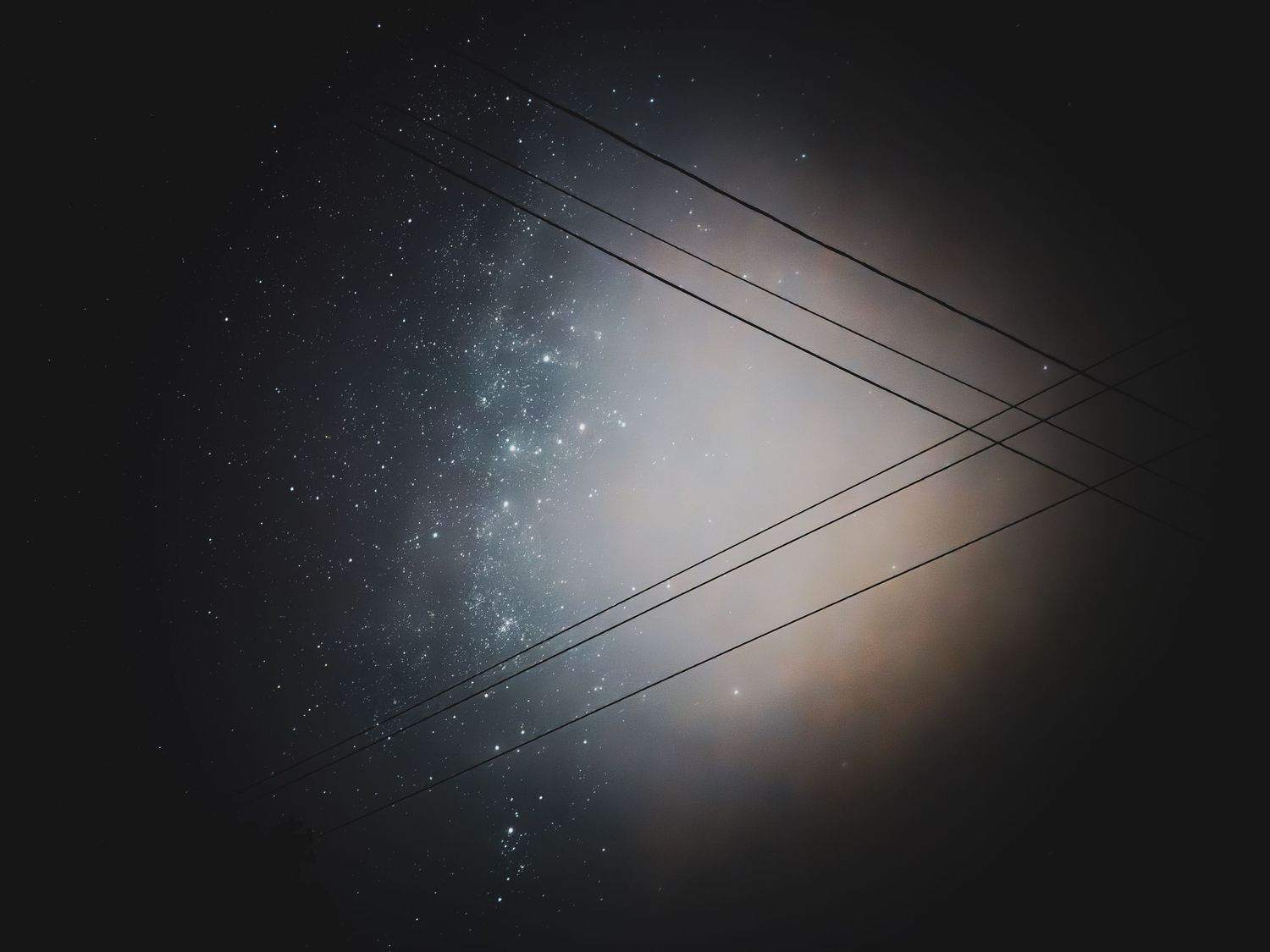 Power lines silhouetted against a starry night sky with glowing lights in the background.