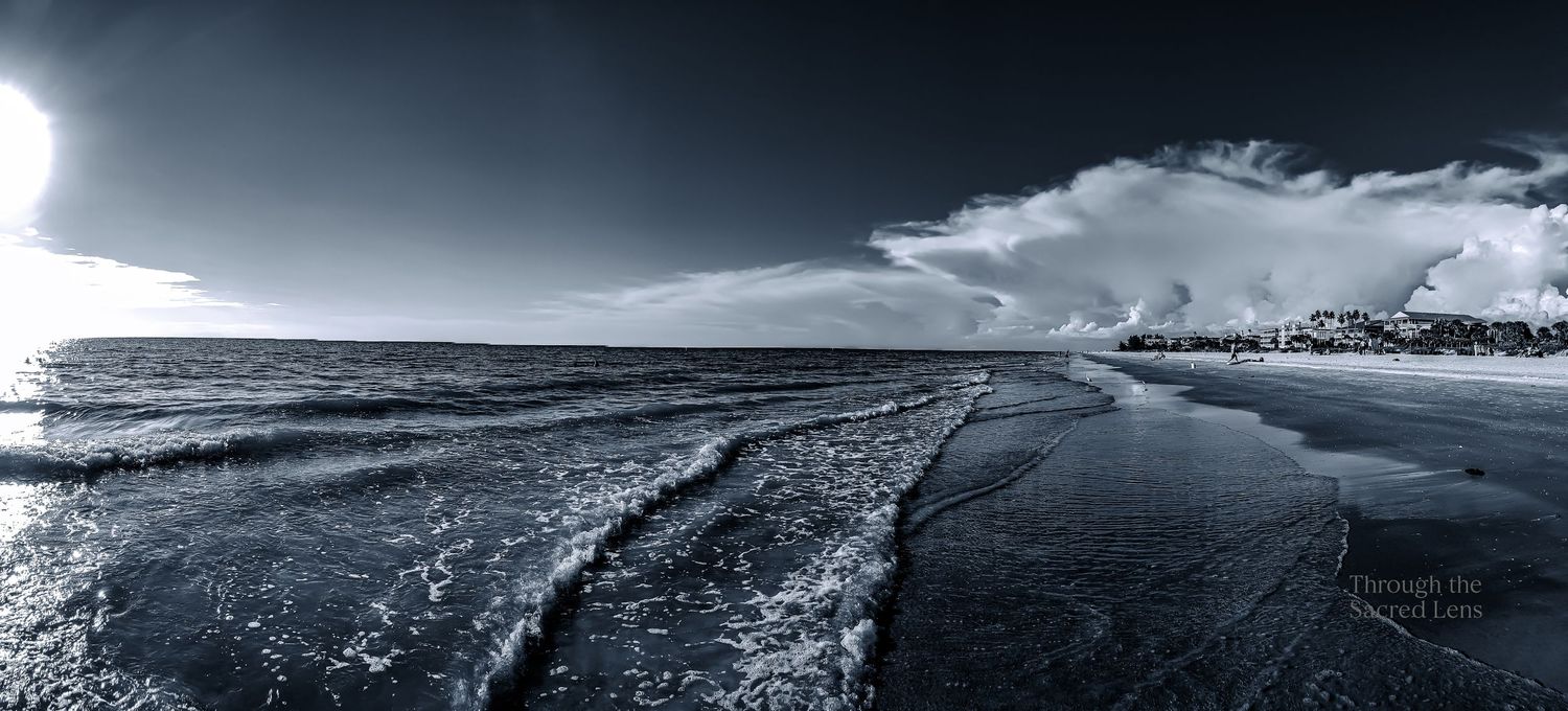 Dramatic black and white panoramic landscape of a rugged coastline under stormy skies.