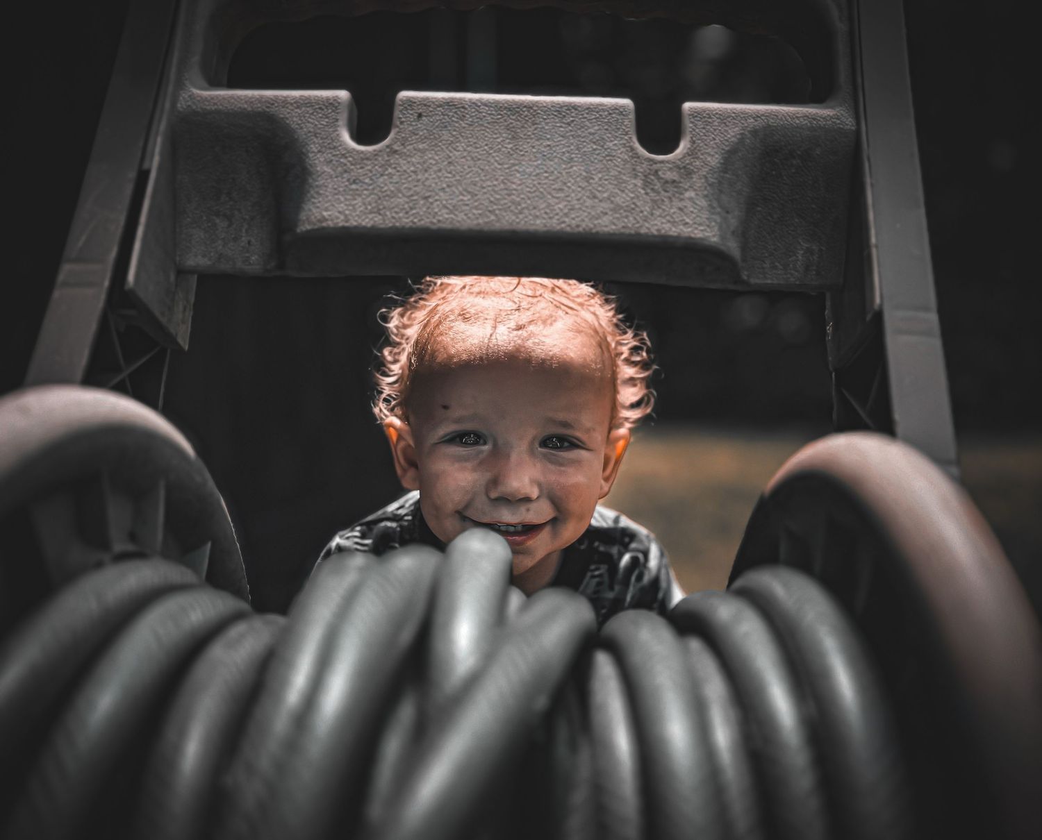 Child peeking through a garden hose  with a playful expression.