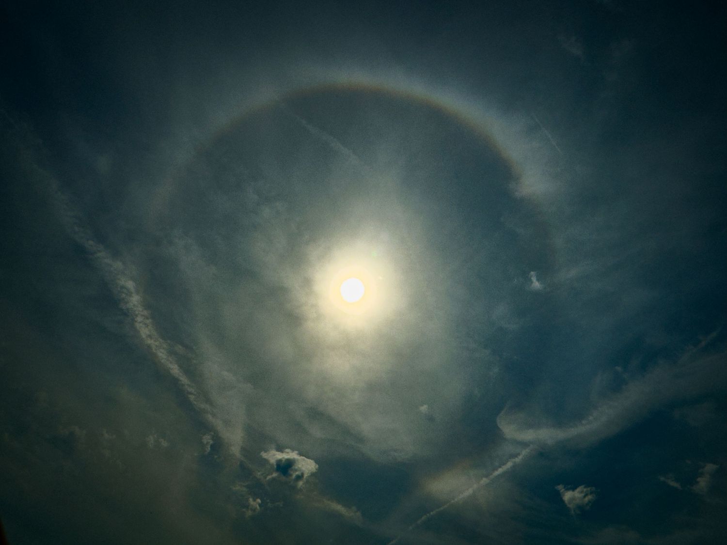 Sun halo phenomenon creating circular rainbow ring in cloudy sky.