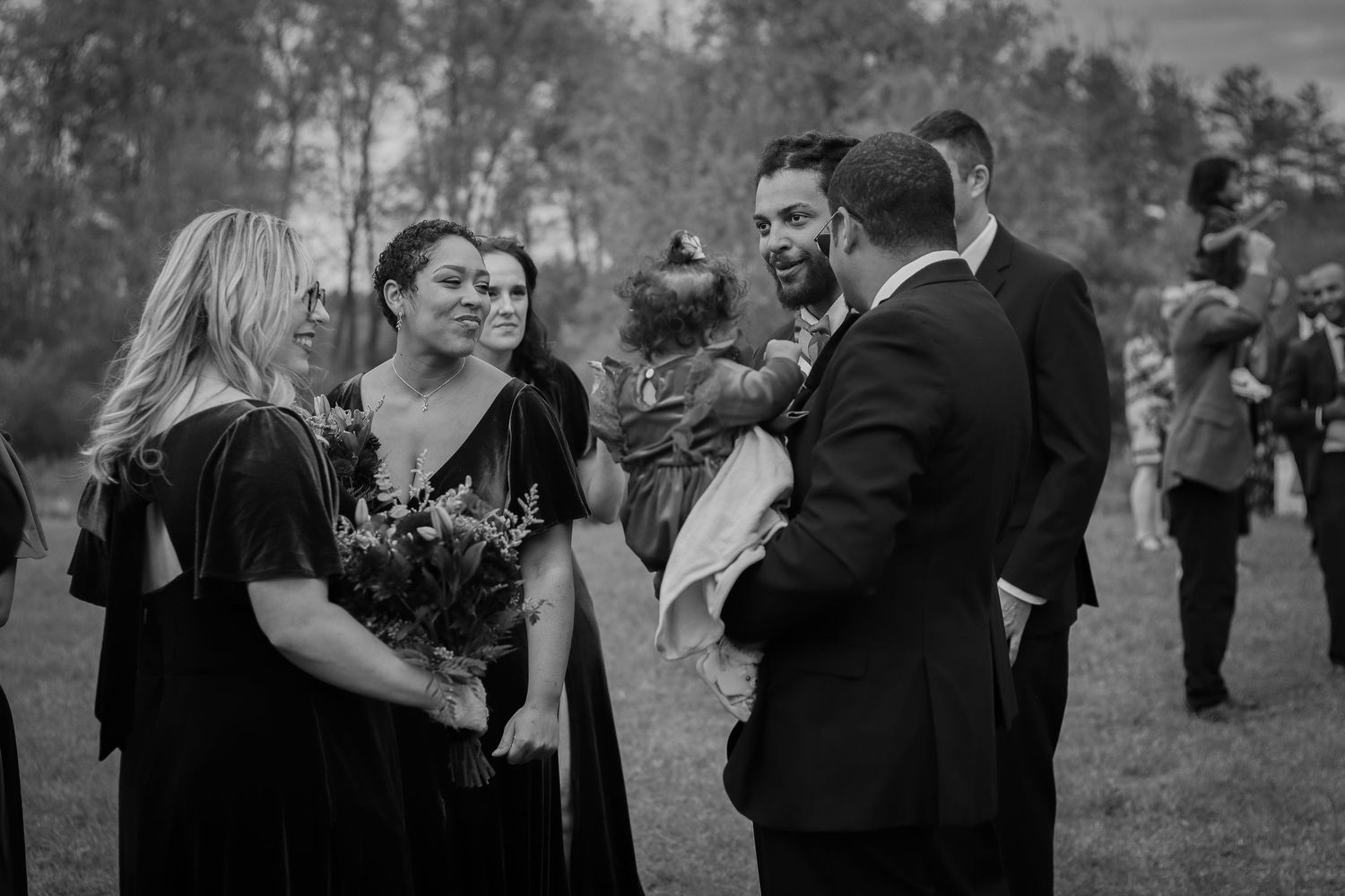 Wedding party members share joyful moments during an outdoor celebration in black and white photography.