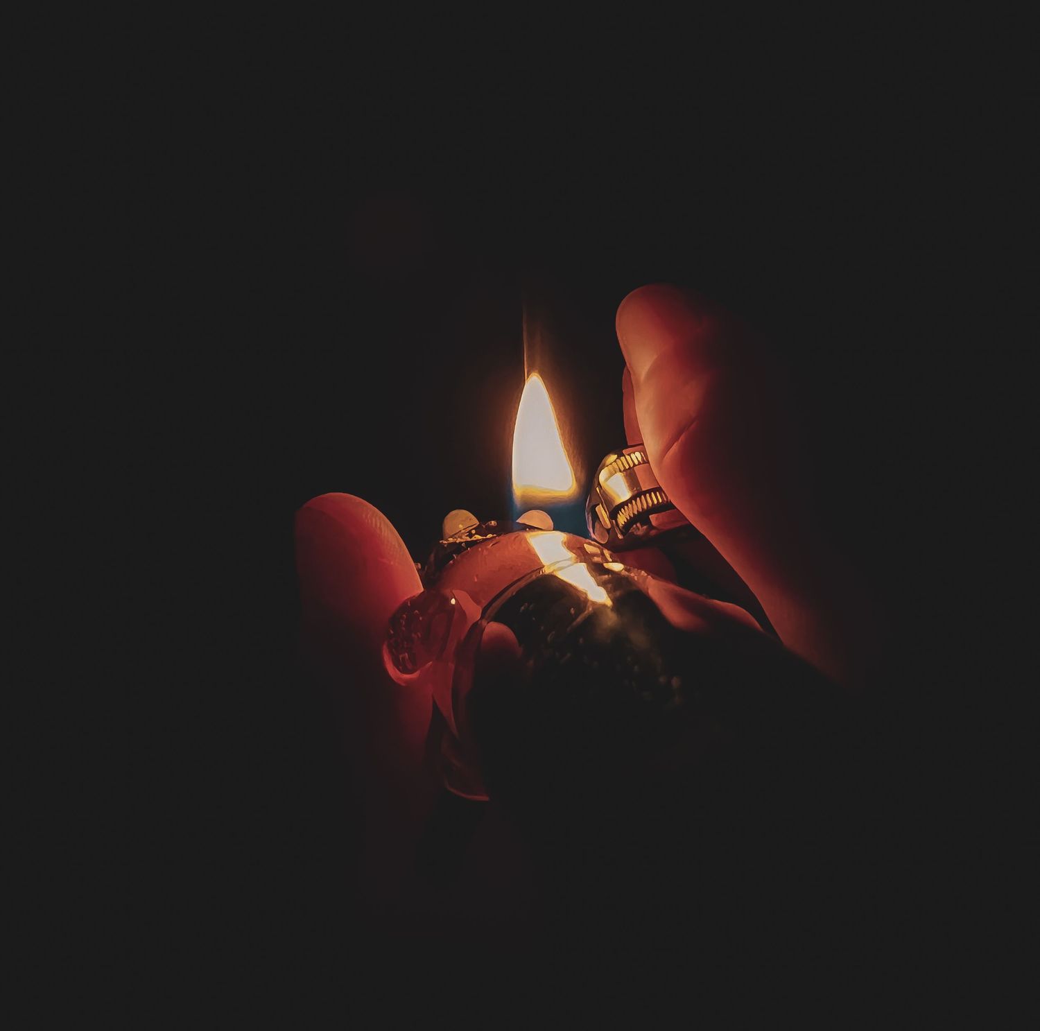 Close-up of hands holding lit lighter in darkness with warm orange glow.
