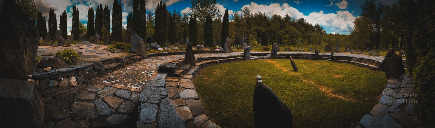 Panoramic view of a mountain landscape with cypress trees and cloudy blue skies.