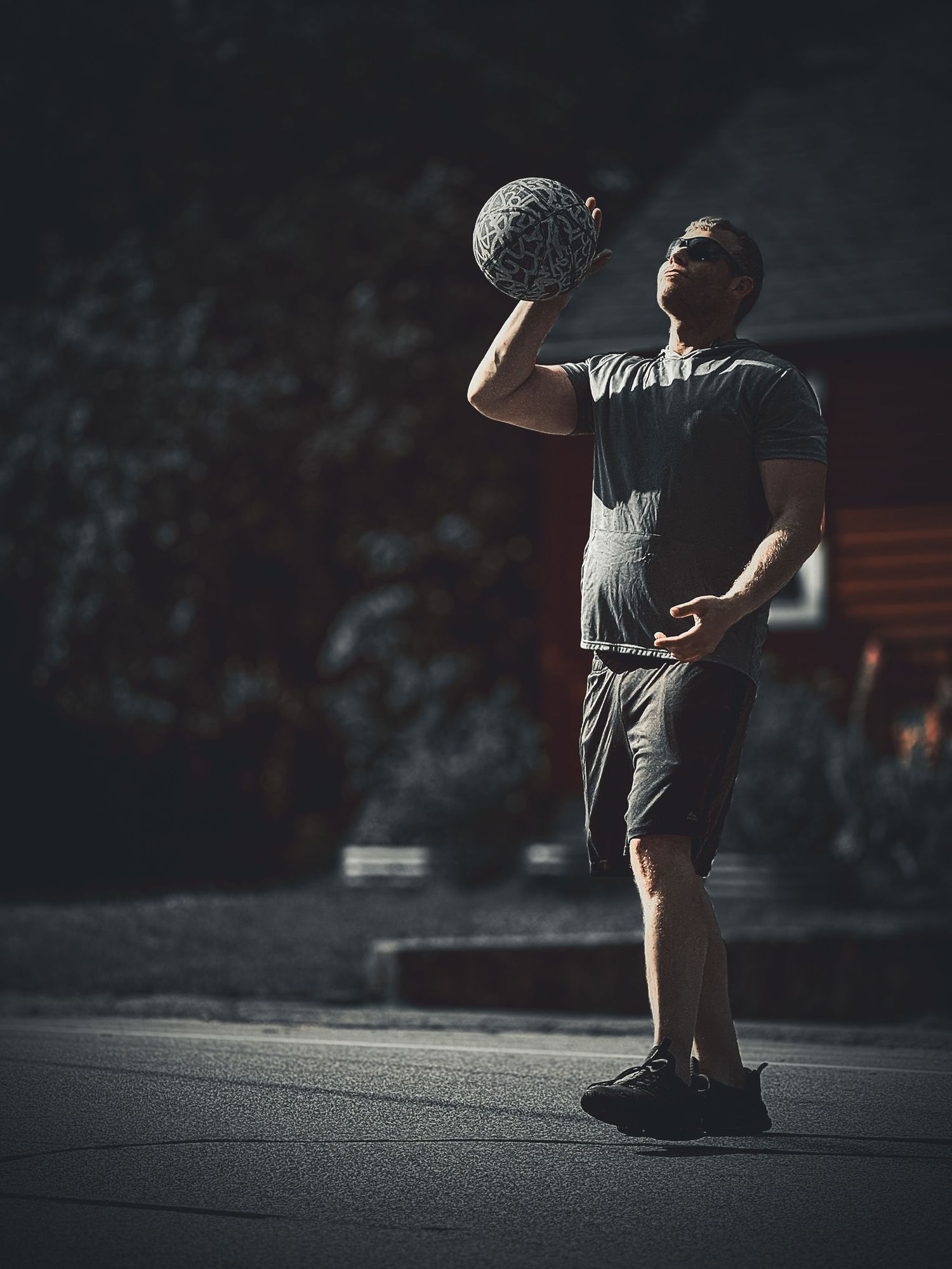 Athletic figure holding a basketball in dramatic lighting on an outdoor court.