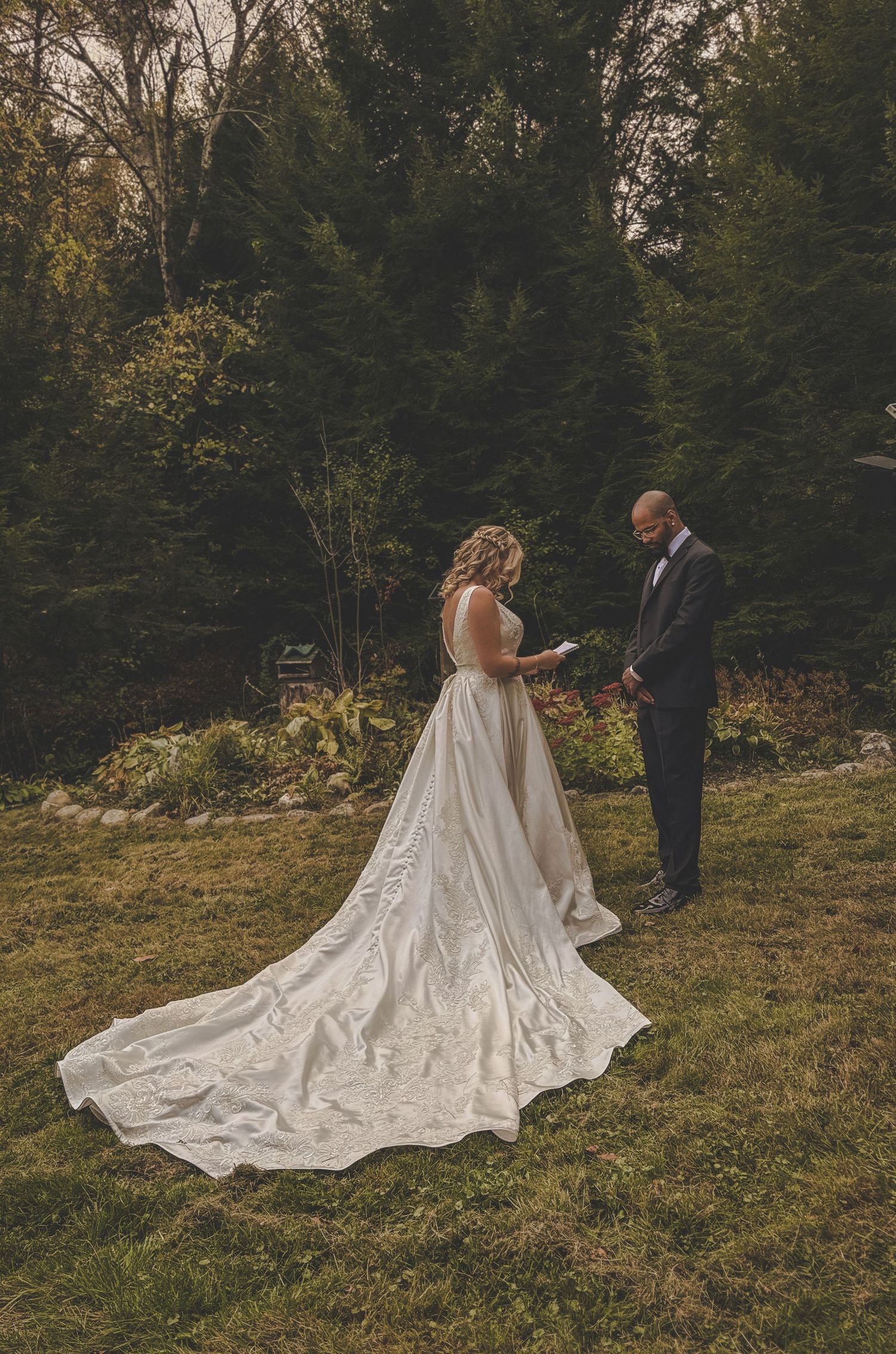 Bride in elegant white gown with long train poses in outdoor garden setting.