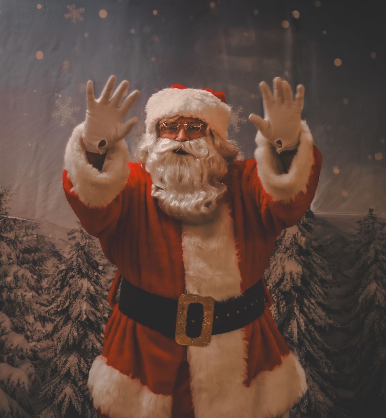Santa Claus raises his hands against a snowy forest backdrop with twinkling lights in a cinematic shot.