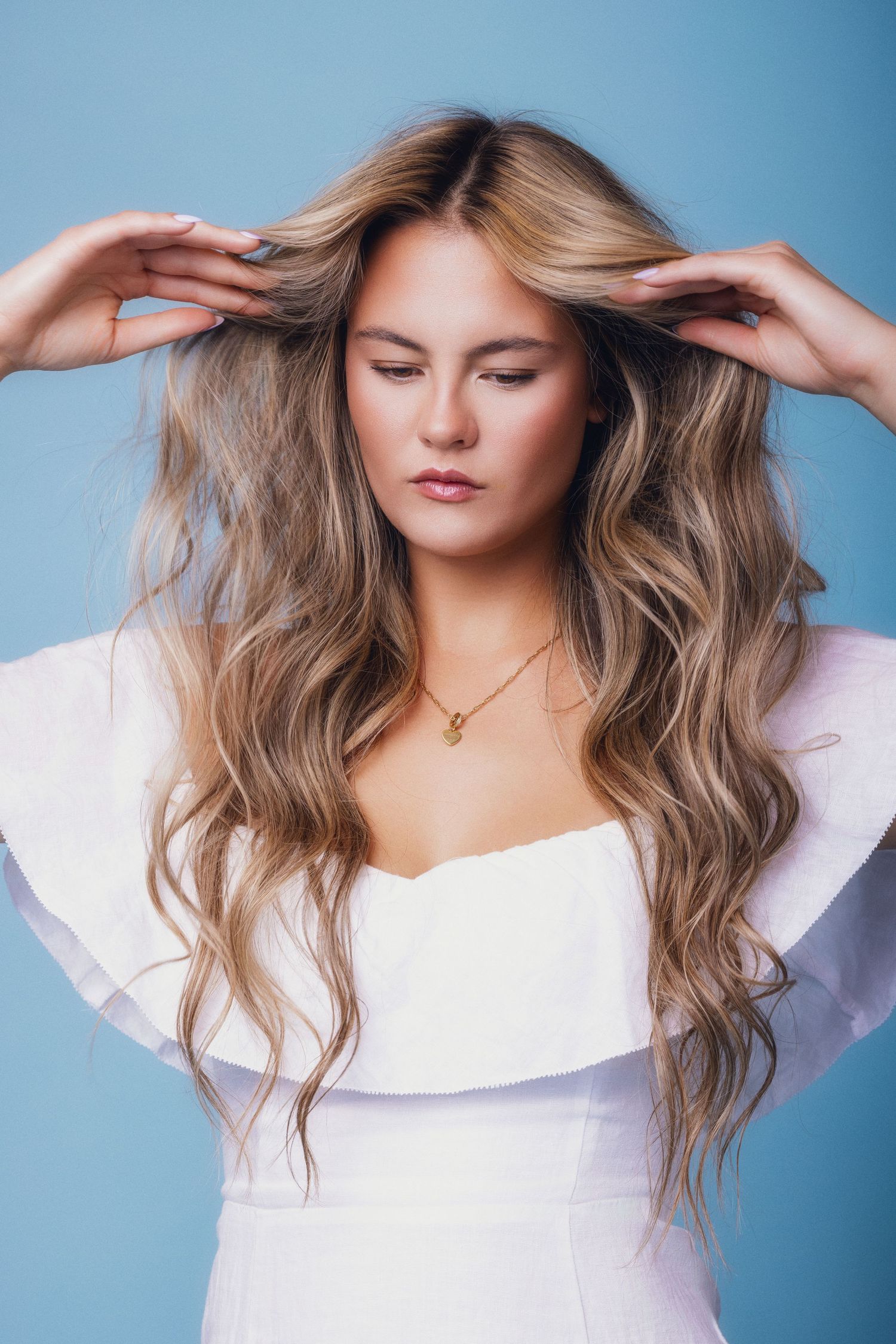 Woman in a white dress lifting her hair against a blue backdrop at a portrait workshop in Canmore.