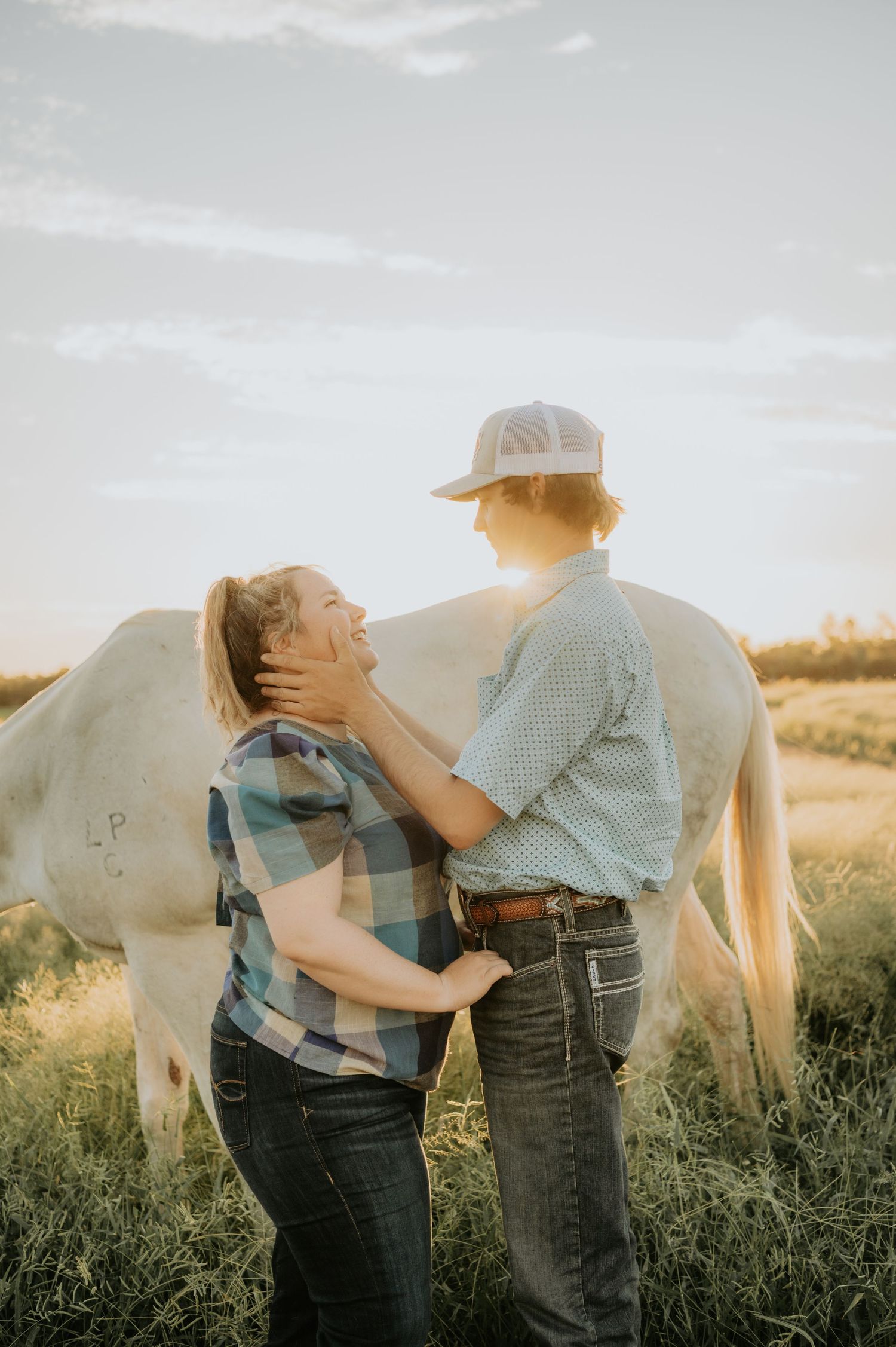 Couple sharing intimate moment near white horse in sunlit field.