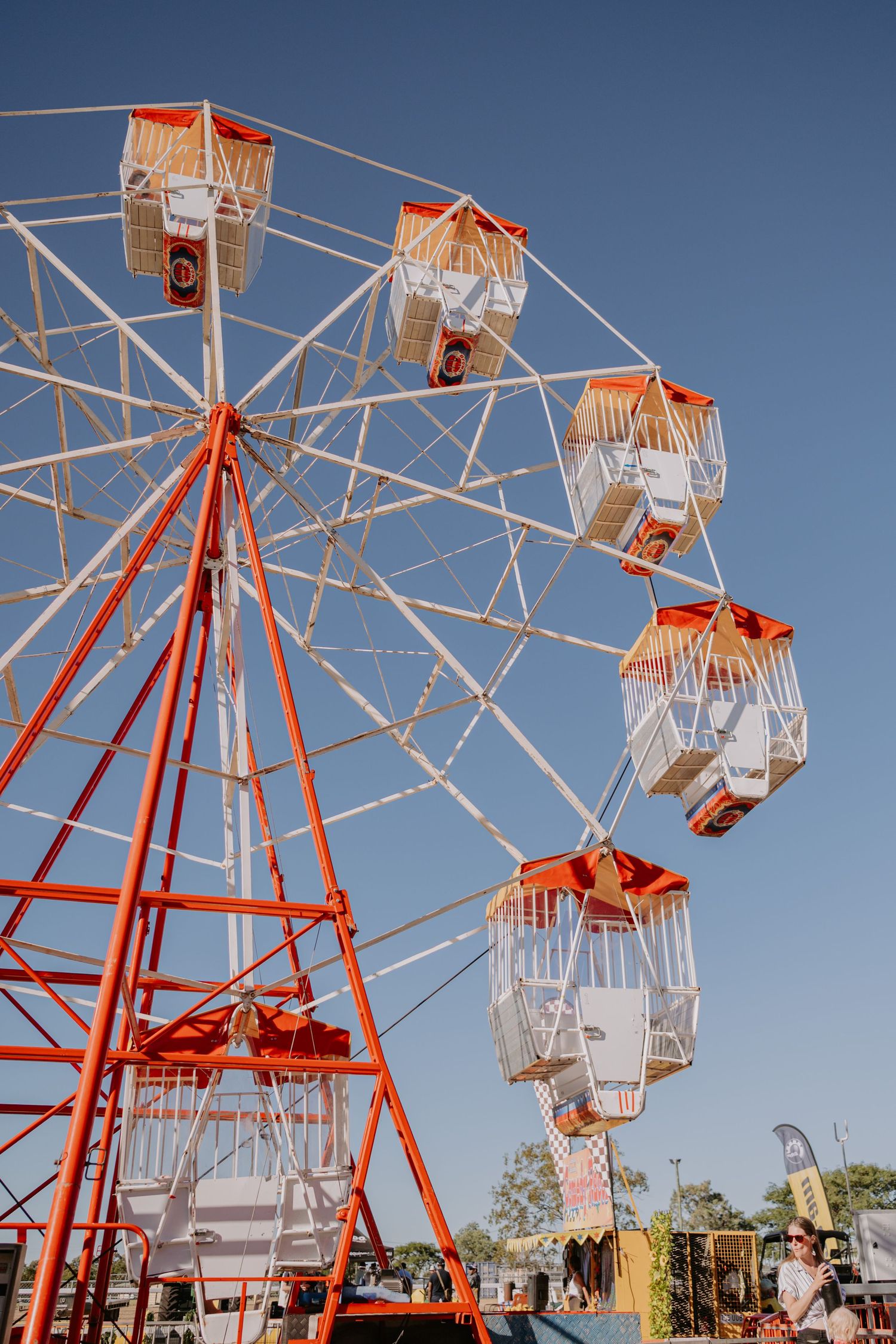 Colorful orange and white ferris wheel against a clear blue sky at an outdoor fairground.
