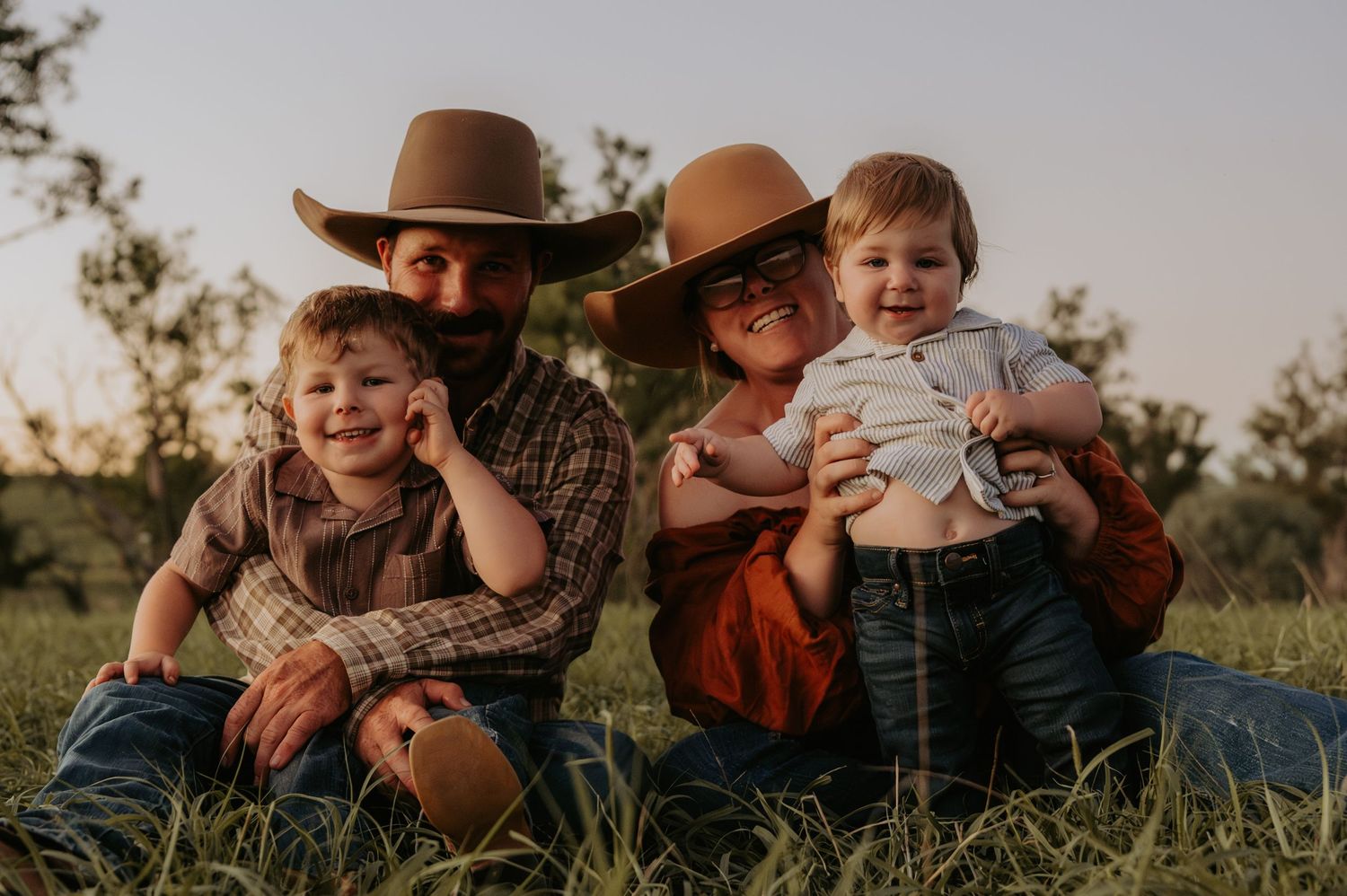 Family sitting together in grass field during golden hour sunset.
