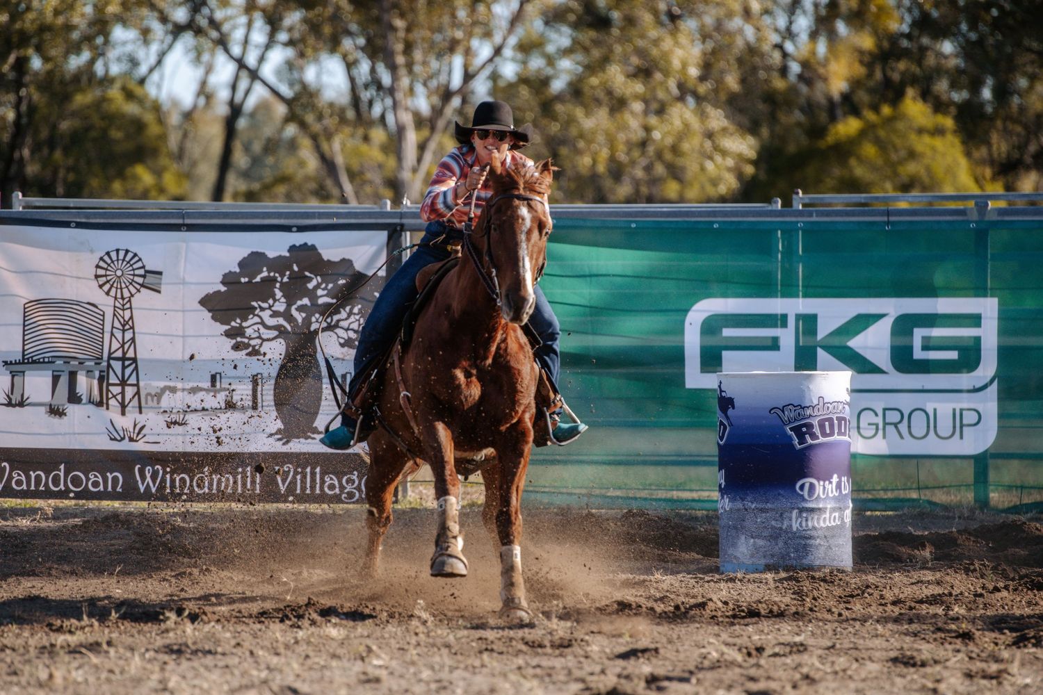 Horse and rider competing in barrel racing at a rodeo event with sponsor banners visible.