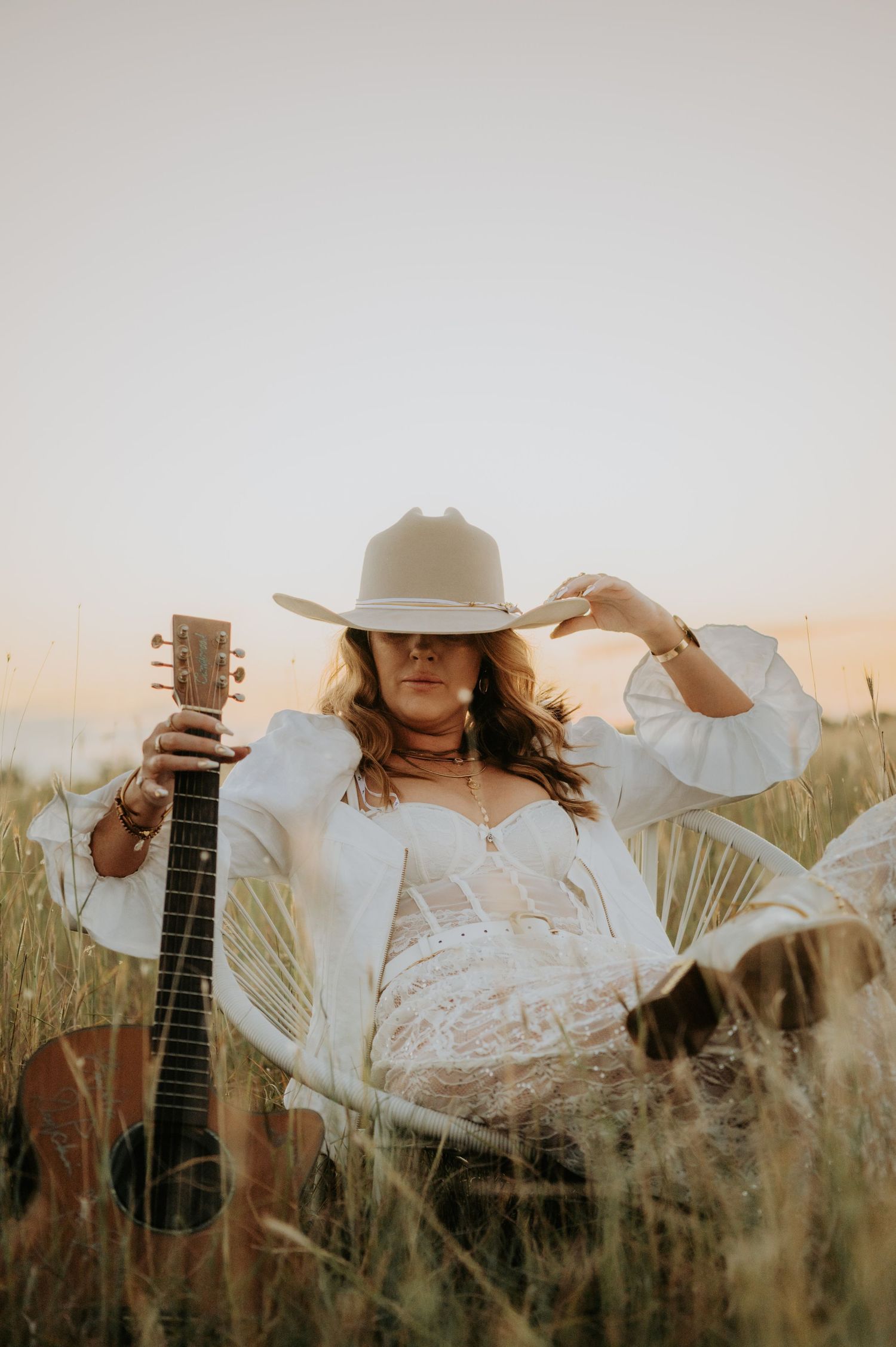 Country western style portrait with guitar and cowboy hat in tall grass.