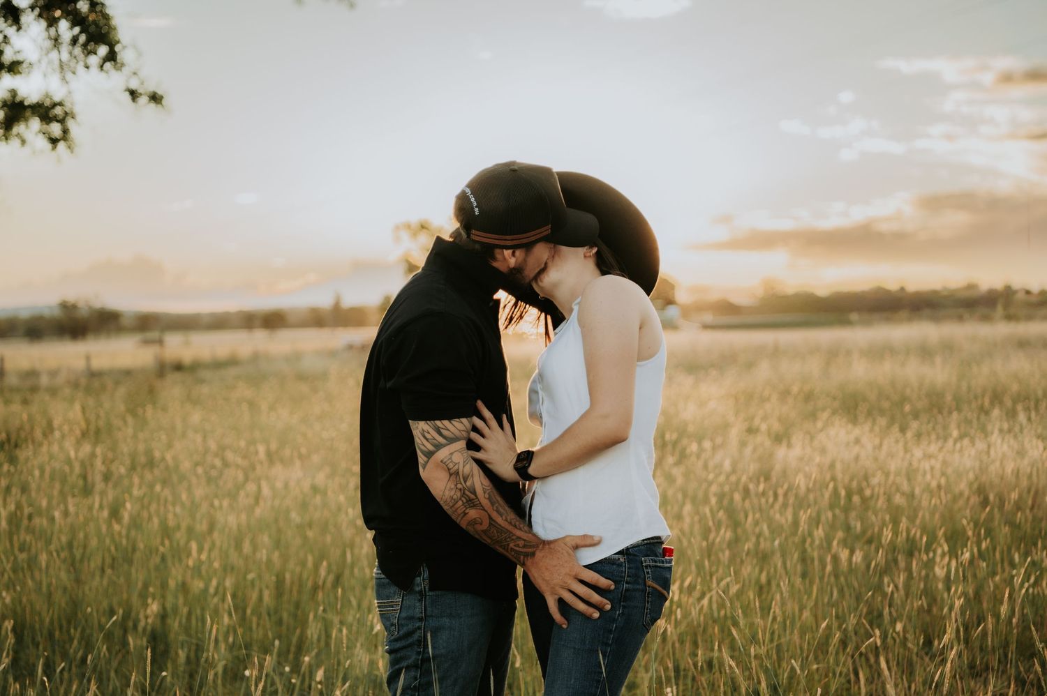 A romantic couple embraces in a golden field during sunset creating silhouettes against the warm sky.