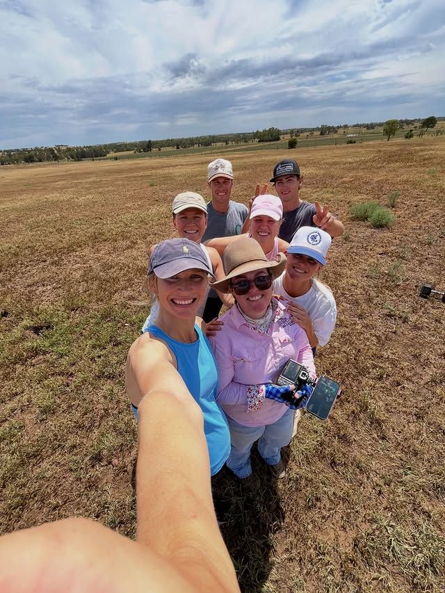 Group selfie taken outdoors in sunny field with blue sky background.