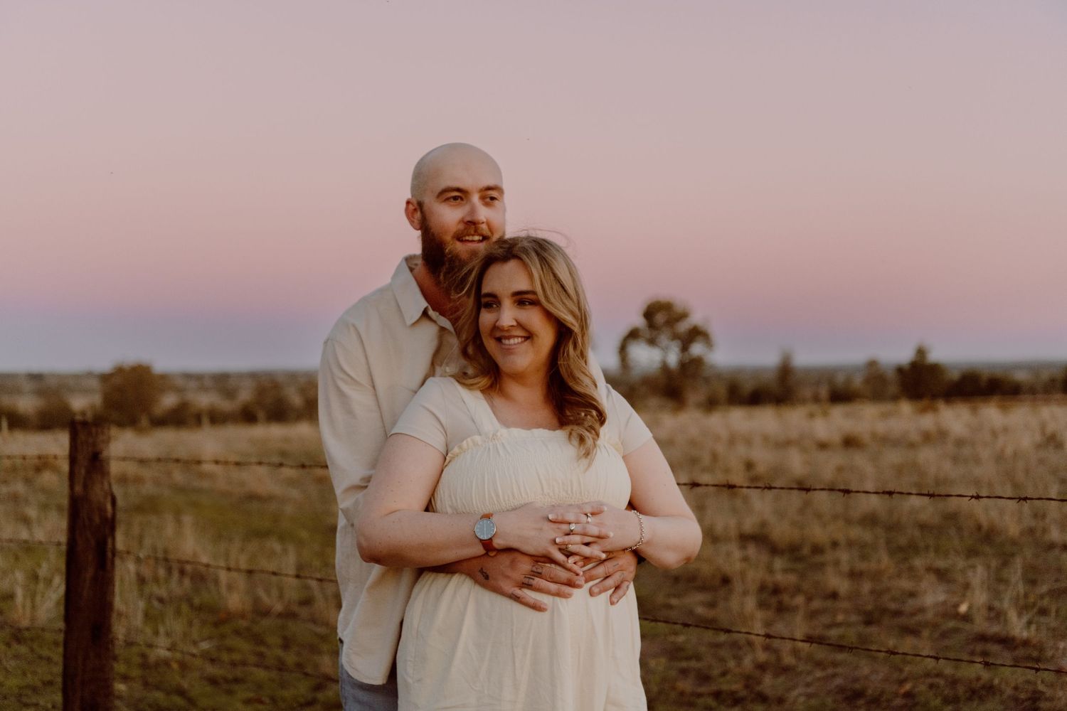 An intimate maternity portrait at dusk with a rustic countryside backdrop.