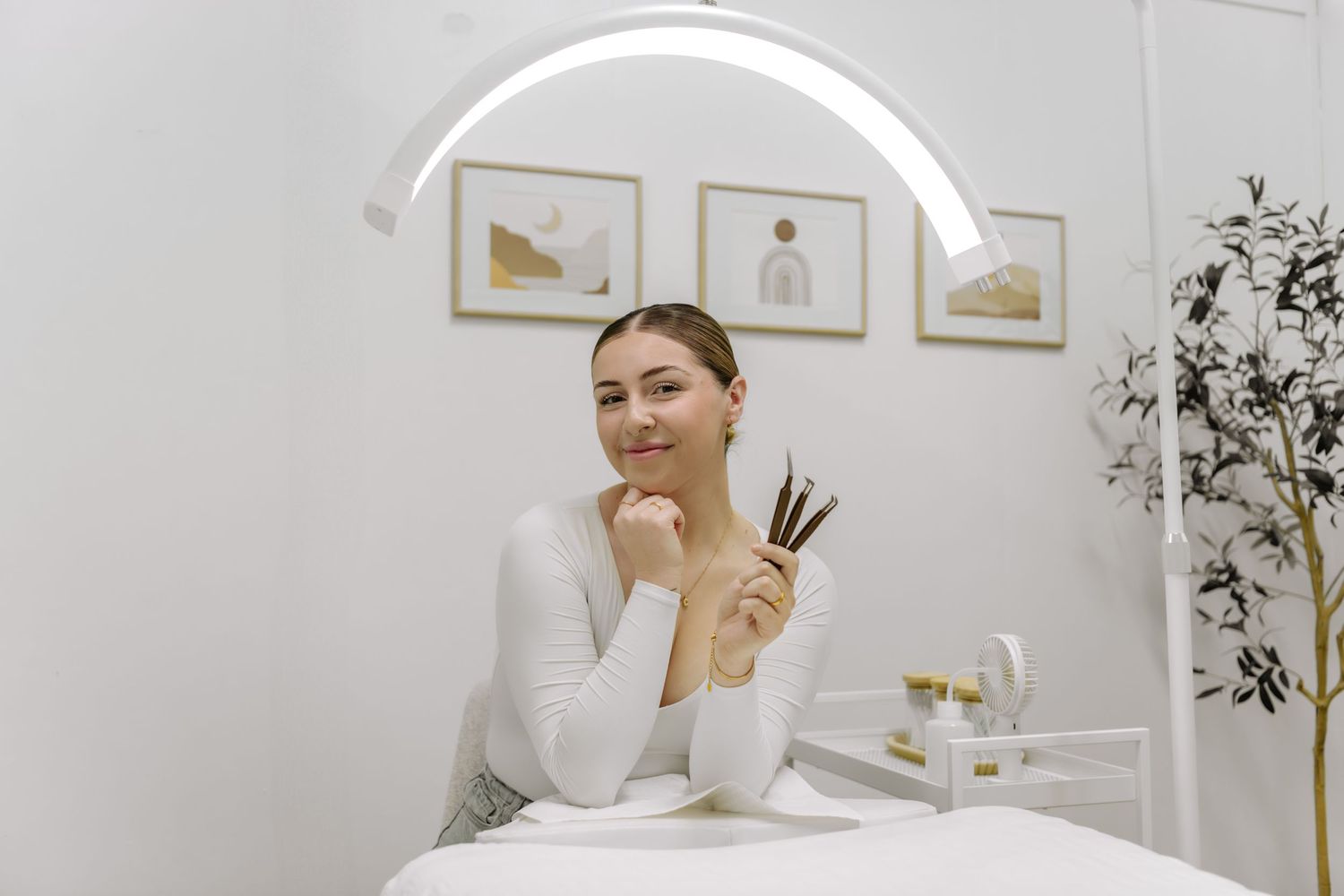 Artist sitting at white desk with art supplies in minimalist studio setting.