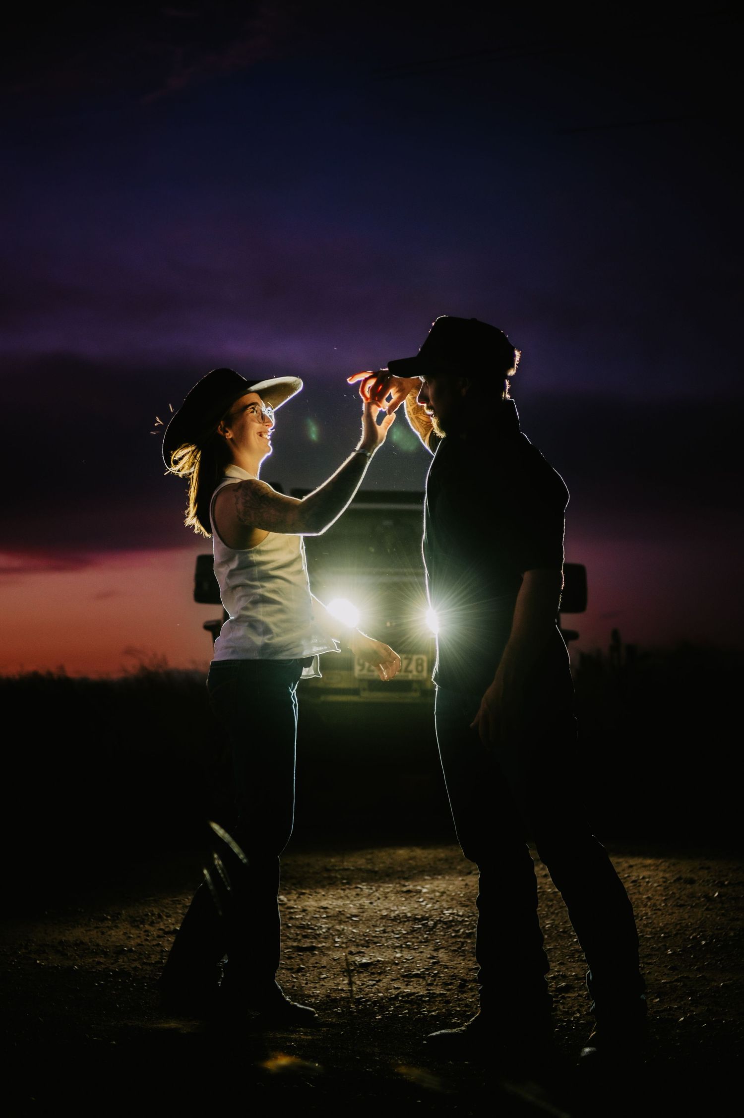 Two silhouetted figures share a romantic moment at sunset with dramatic backlighting creating a glowing atmosphere.