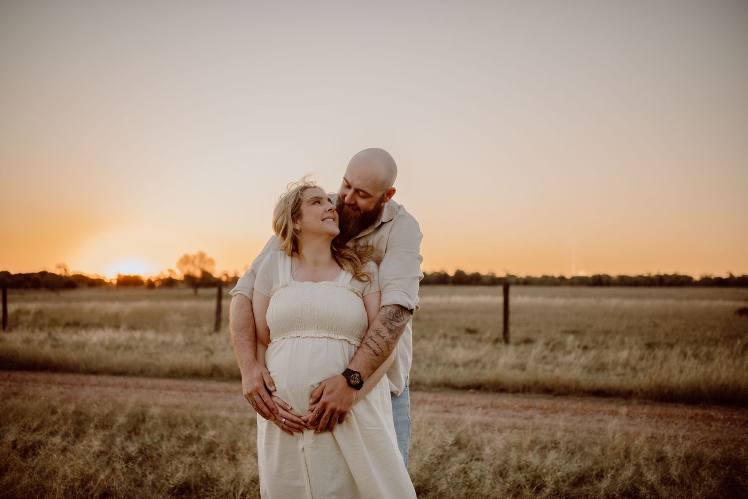 A romantic maternity photoshoot in a field at golden sunset with soft lighting and warm tones.