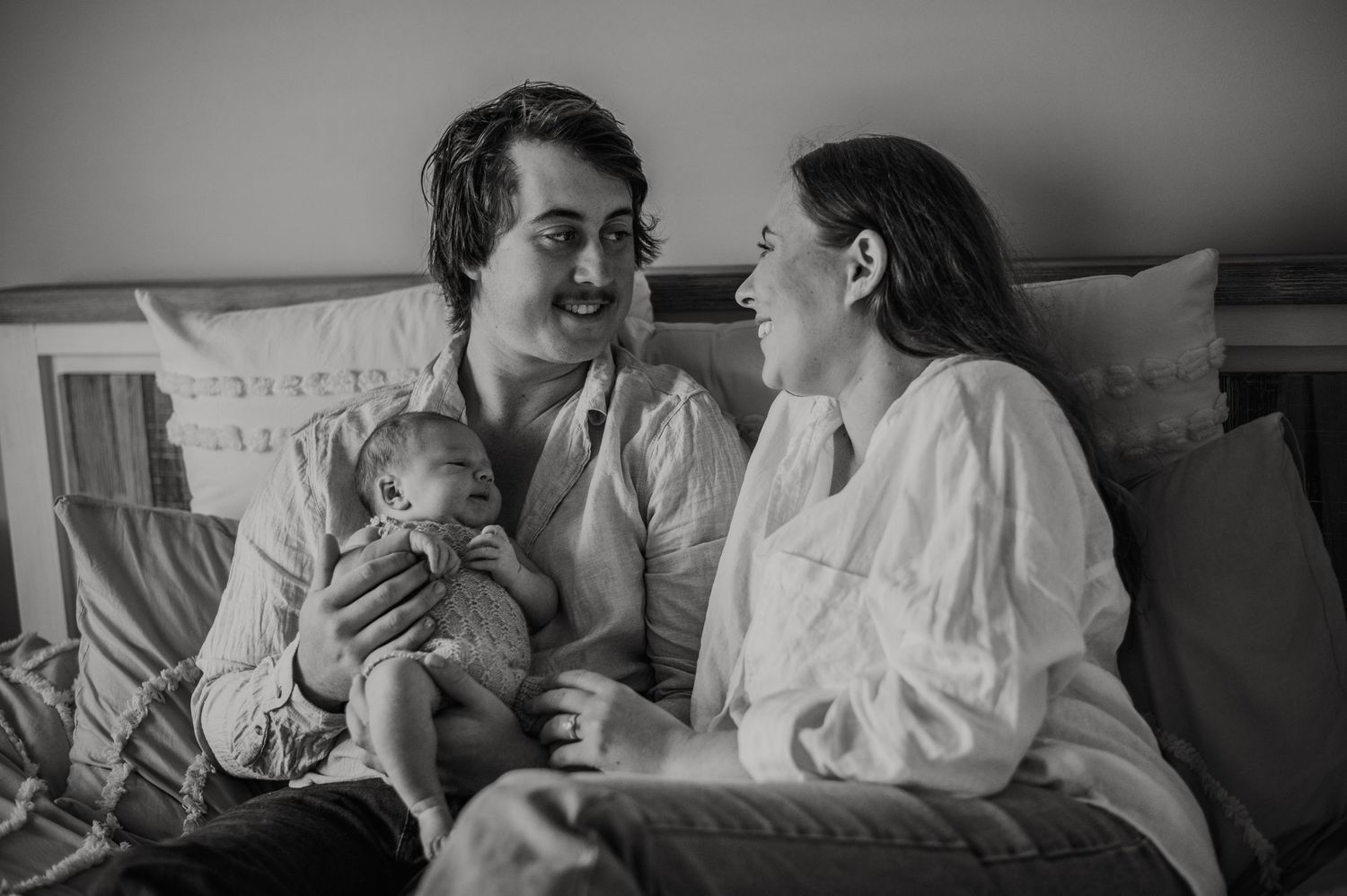 Black and white lifestyle photography showing intimate family moments on white bedding.