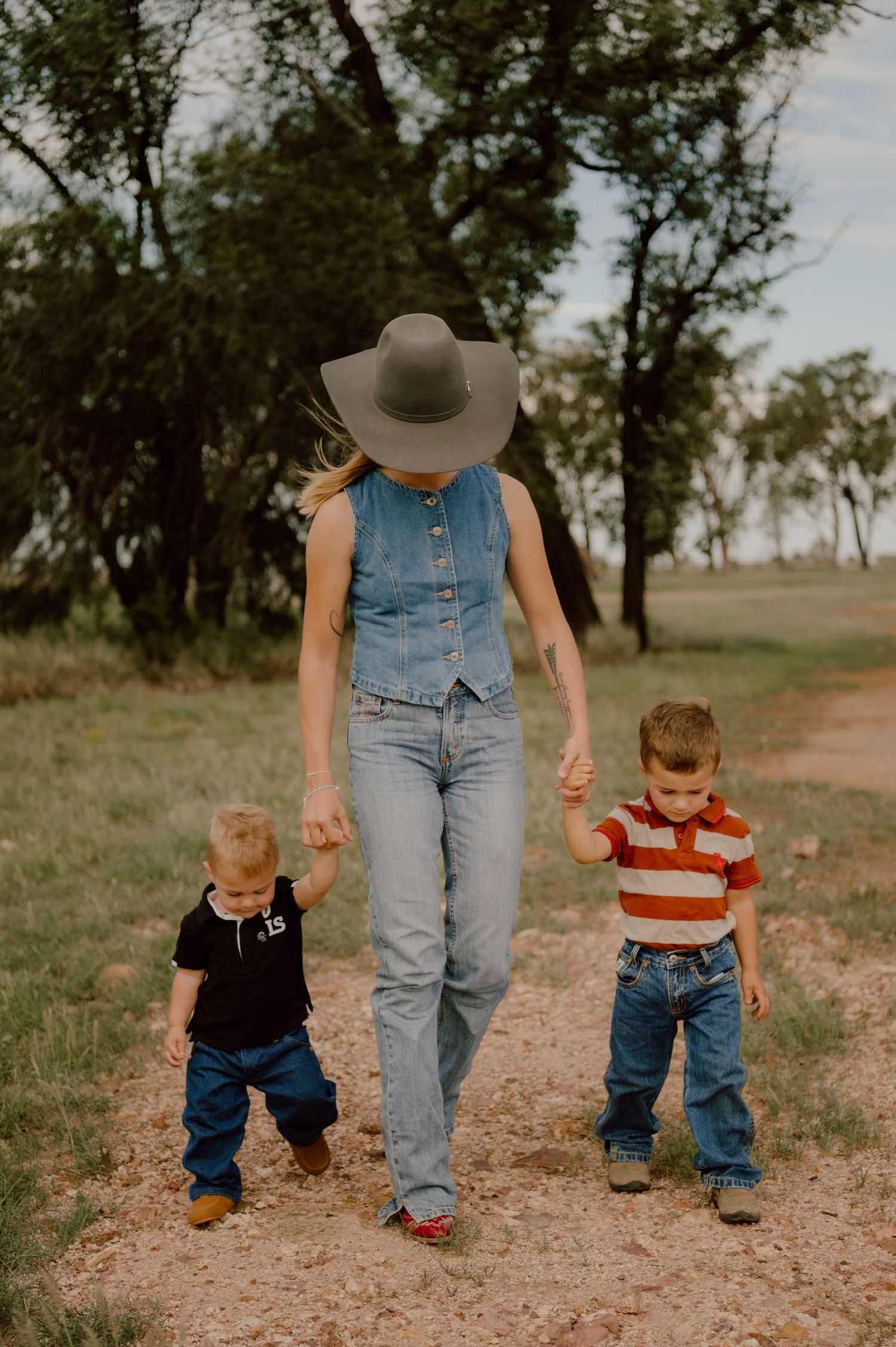 A parent and toddlers walking together on a dirt path through rustic countryside.