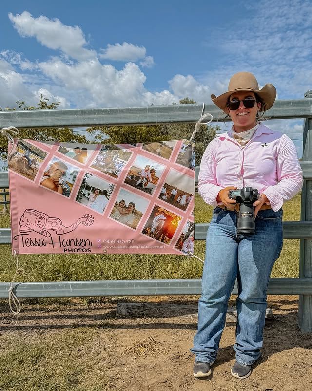 Photographer displays pink photo prints while sitting on wooden fence outdoors.