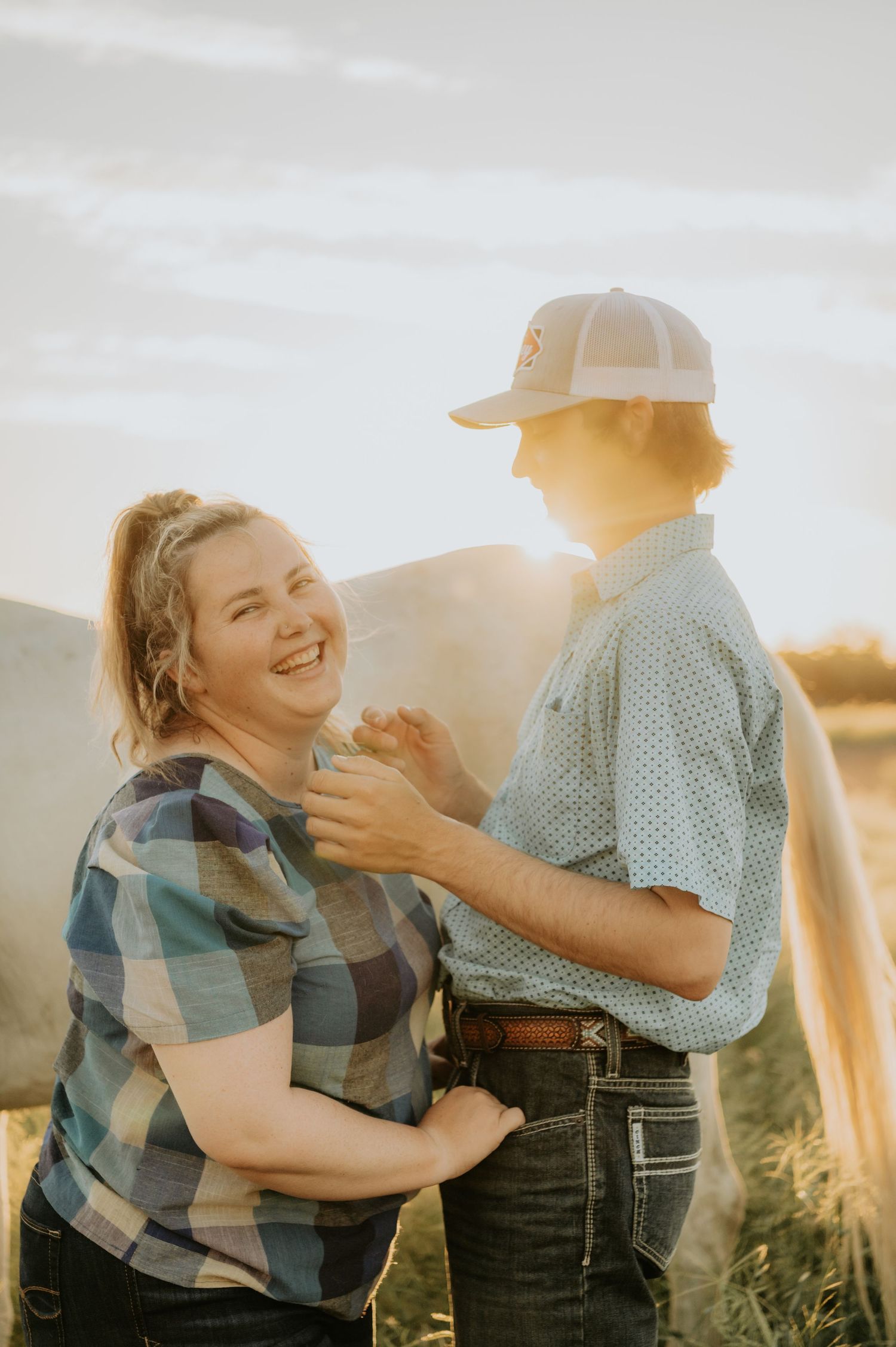 A couple shares an intimate moment while laughing together in golden hour sunlight.