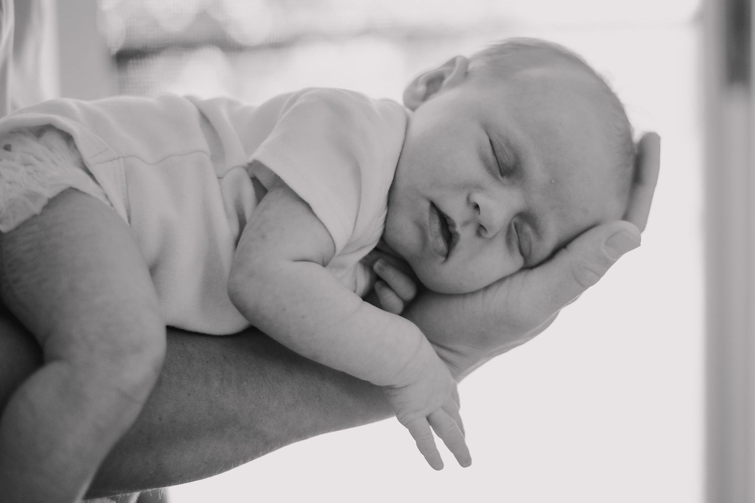 Black and white image of sleeping baby resting peacefully on adult's arm.