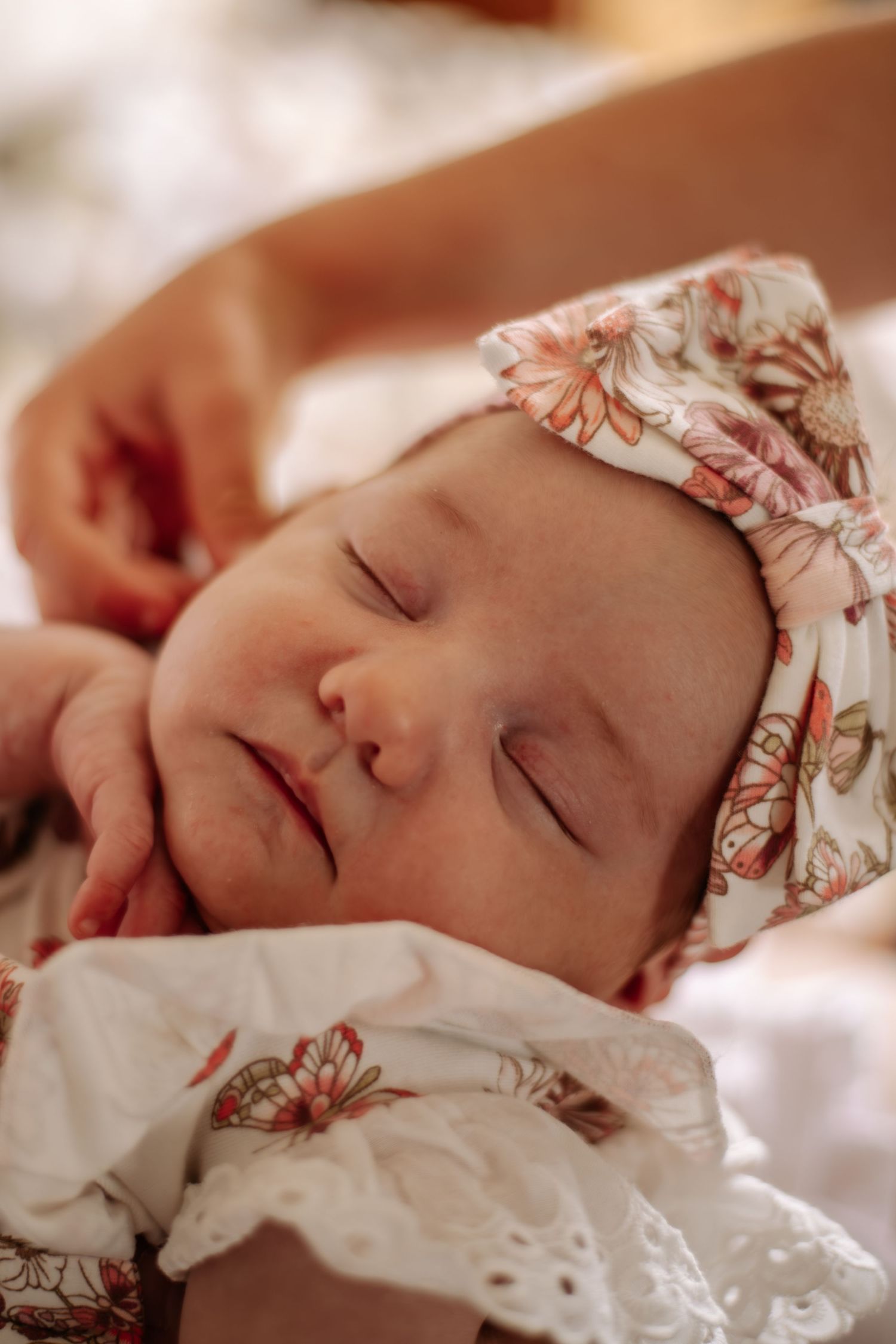 Sleeping newborn in floral outfit captured in soft, warm tones during lifestyle session.