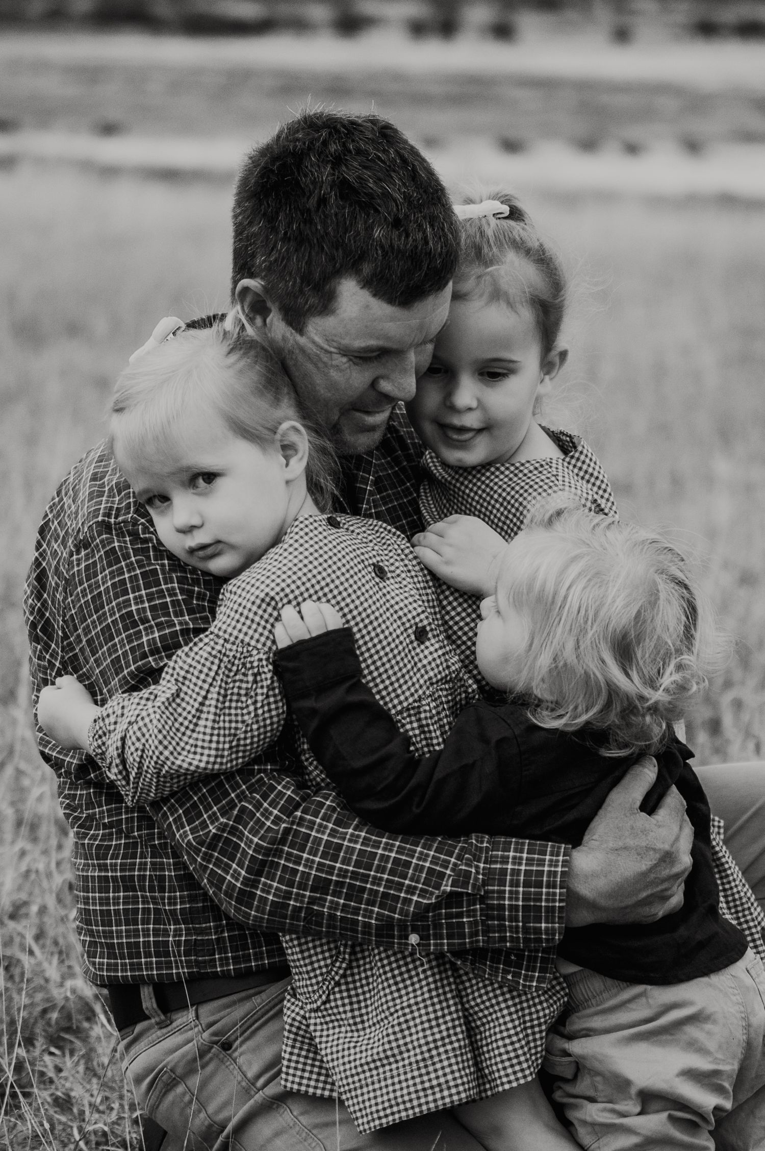 Black and white photo of a father hugging three young children in a grassy field.