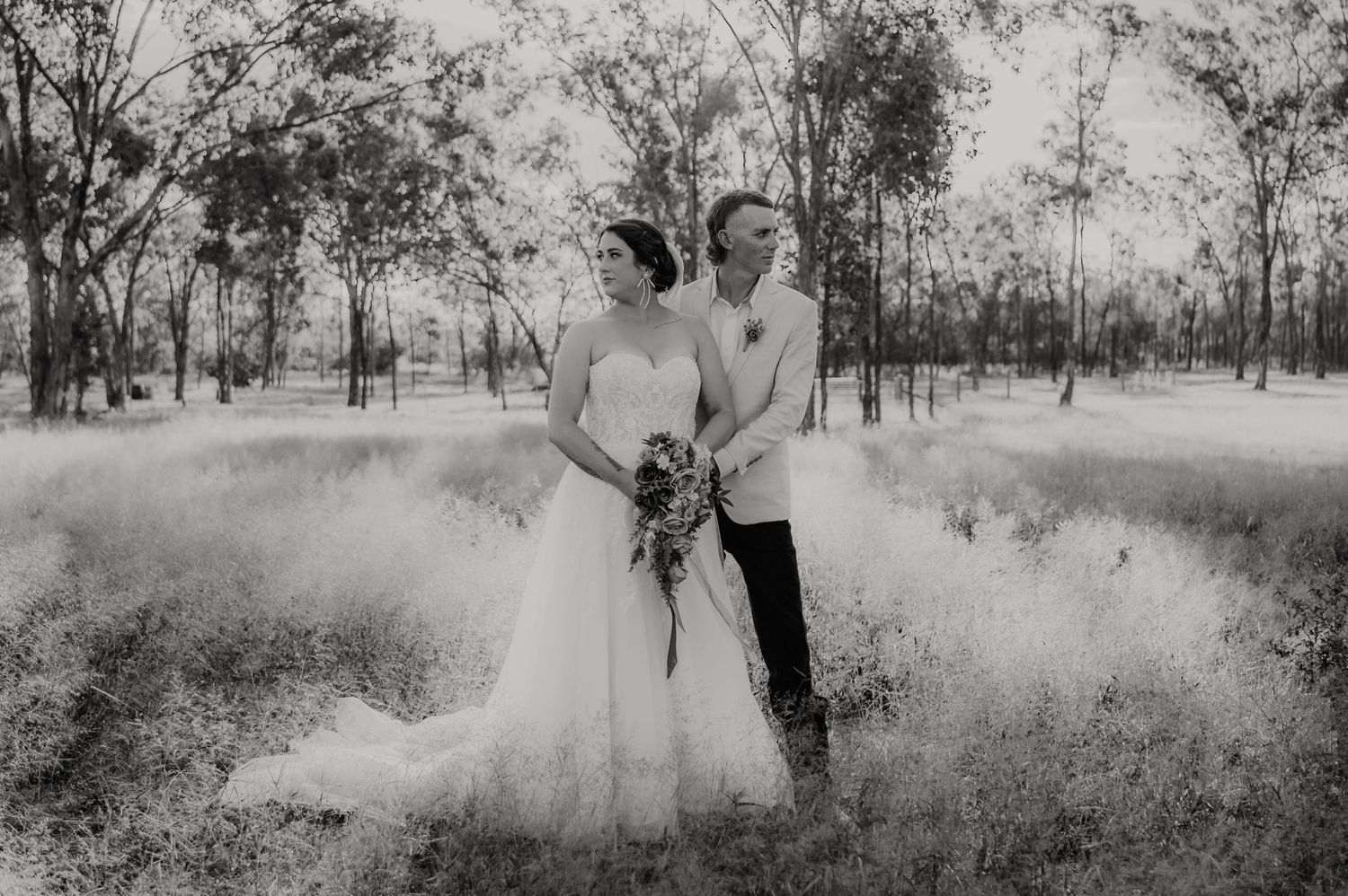 Black and white wedding photo of bride and groom standing in a field surrounded by trees in Australia.