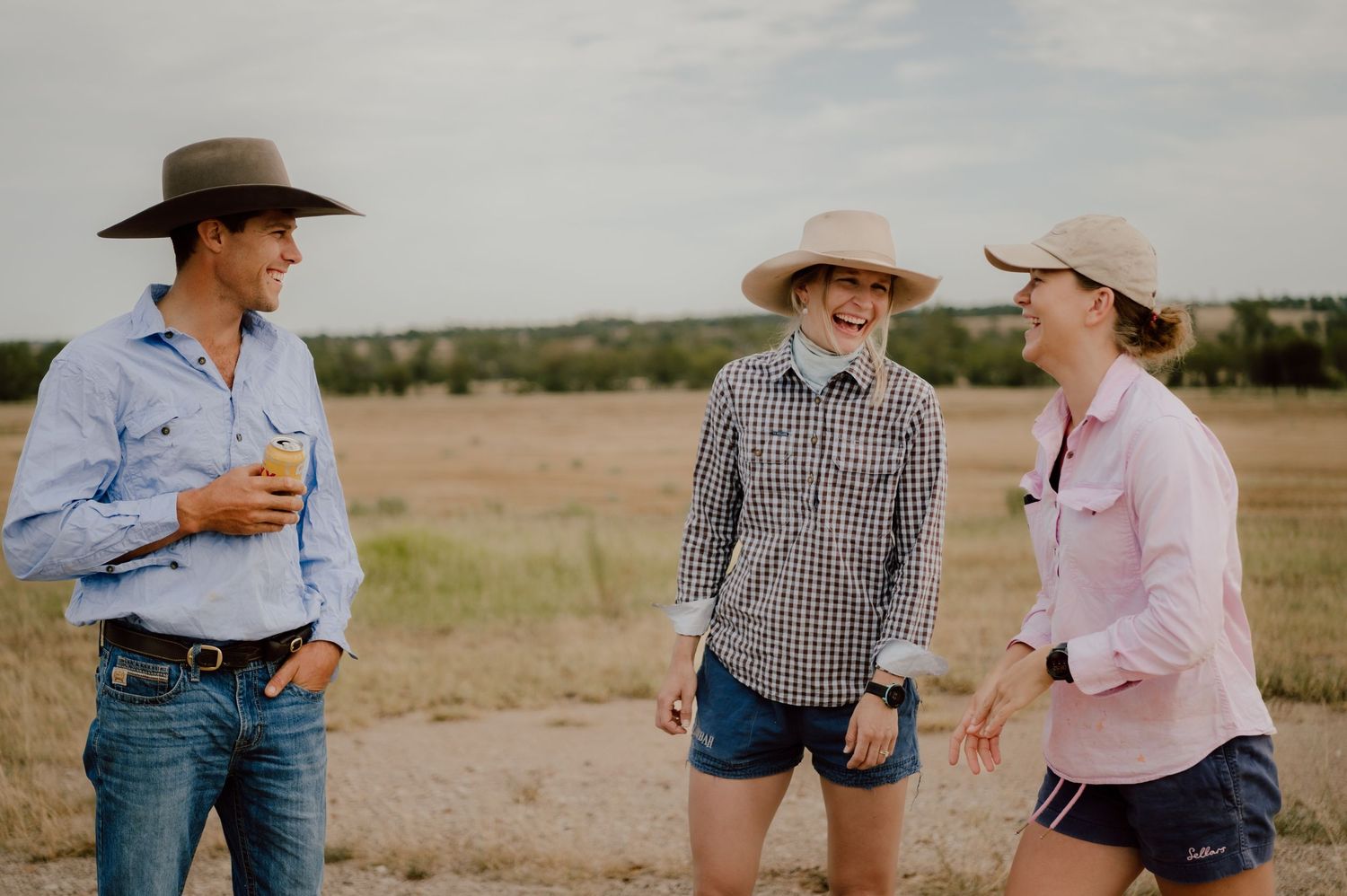 Group of people in western attire having a conversation in an outdoor field setting.