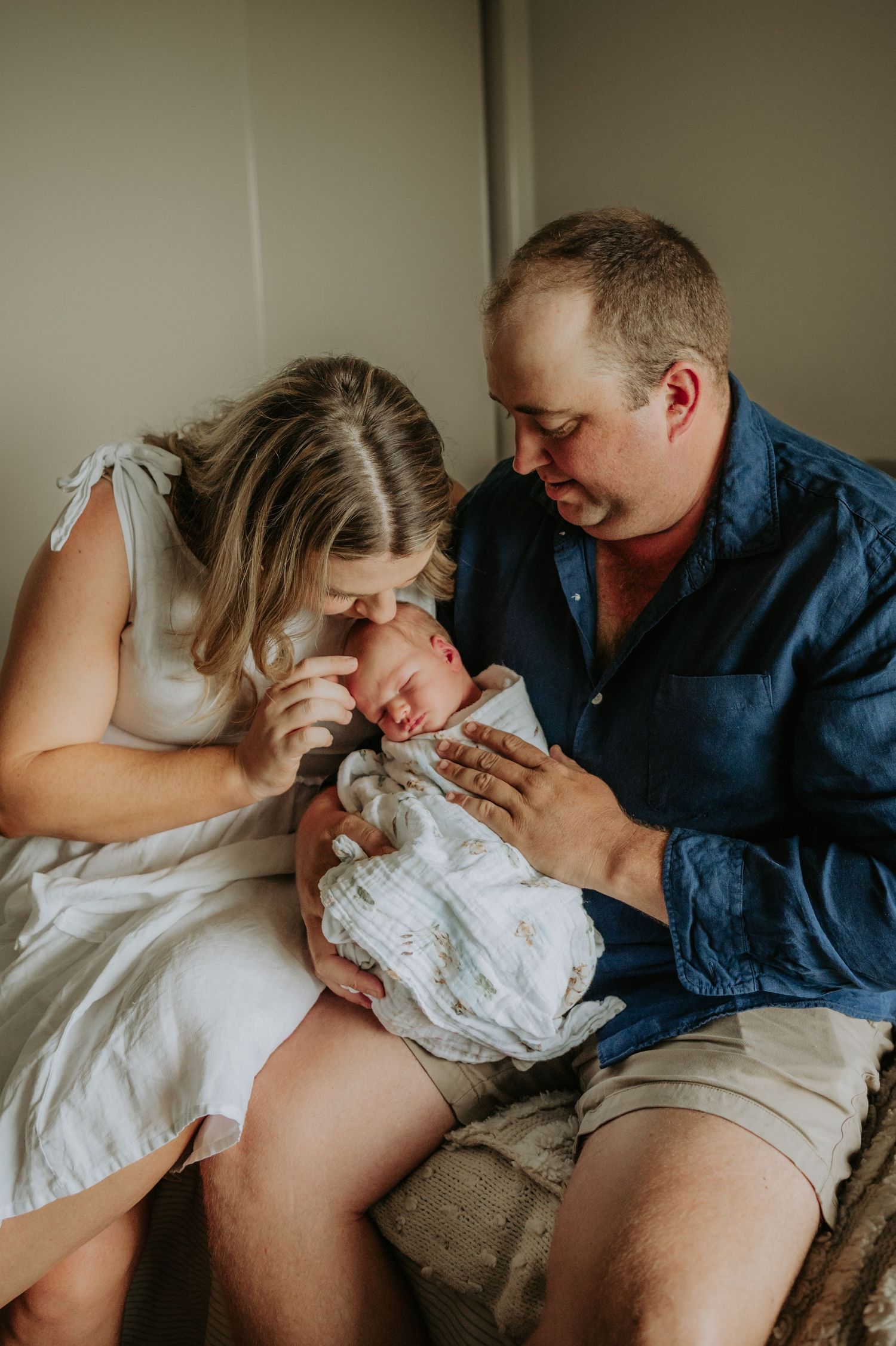 New parents tenderly cradling their swaddled newborn baby together, sharing a precious intimate family moment.